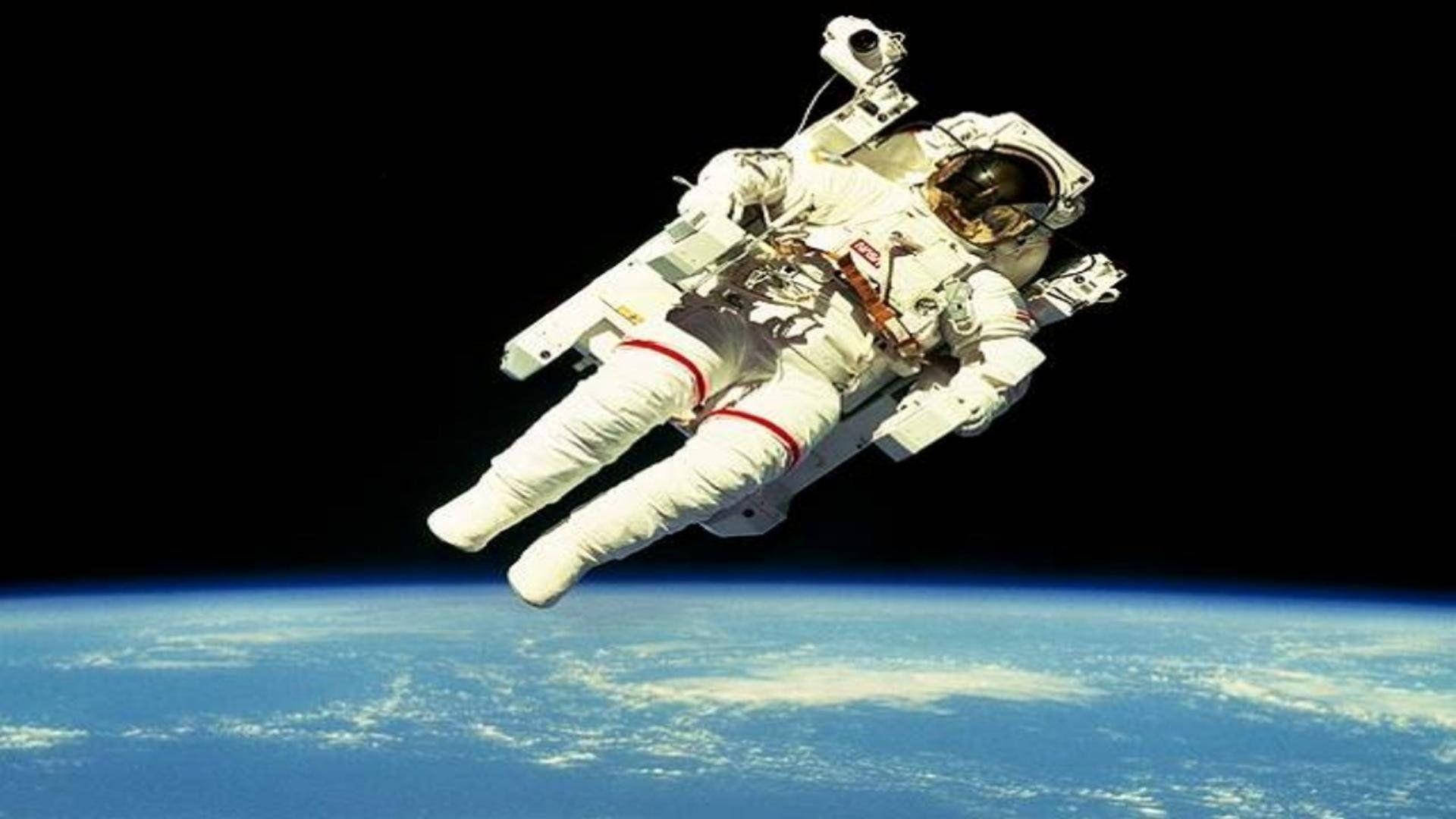 地球 桌布 壁紙 — 一名太空人在零重力下漂浮在地球藍色彎曲地平線之上，背景是太空的黑色虛空。