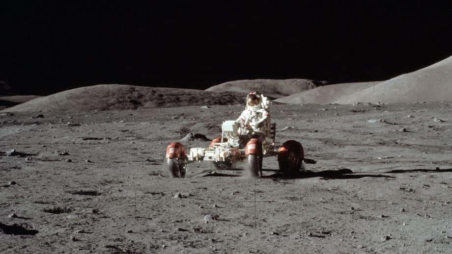 Lunar Rover 桌布 壁紙 — 一名太空人在黑色天空下駕駛月球車穿越荒蕪的灰色月球表面。