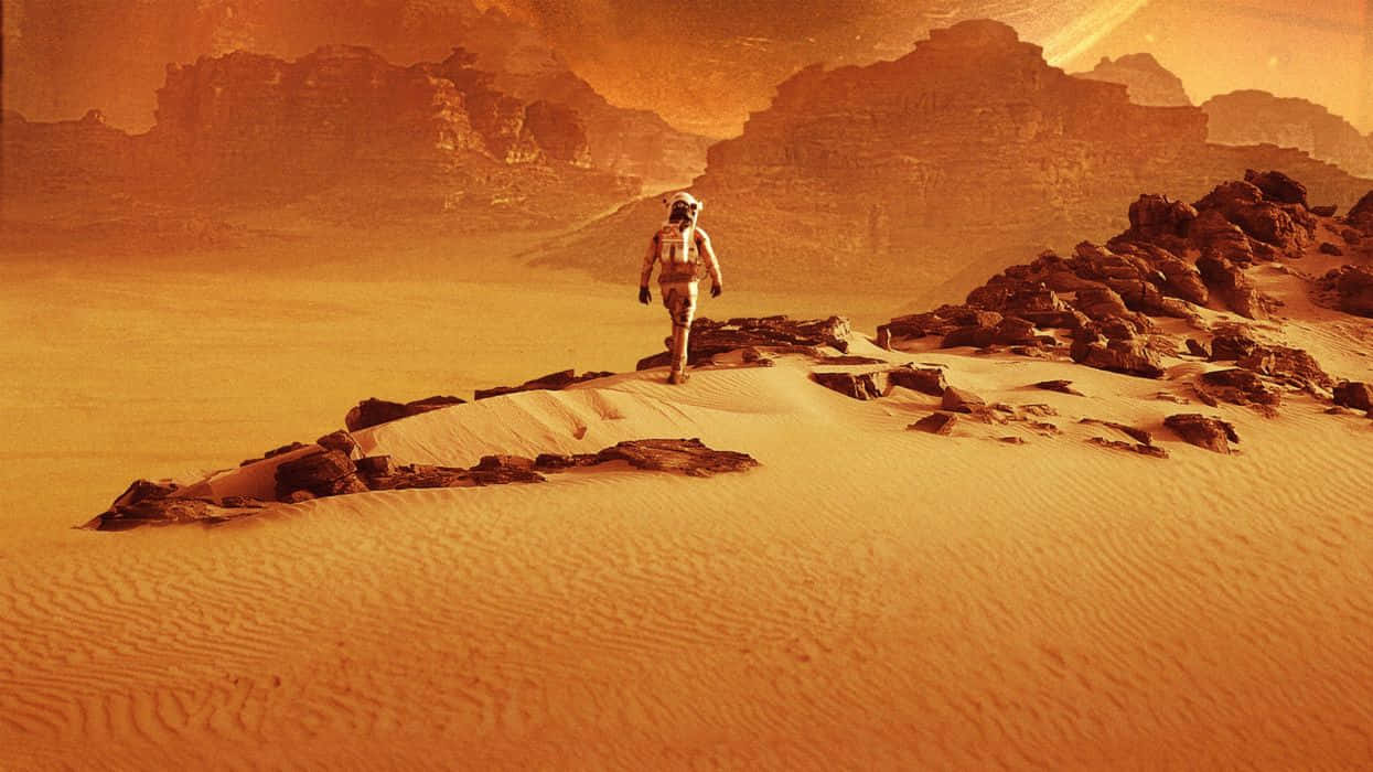 Mars Landscape 桌布 壁紙 — 一名太空人獨自穿越火星廣闊的橙色沙漠，地形崎嶇，天空朦朧。