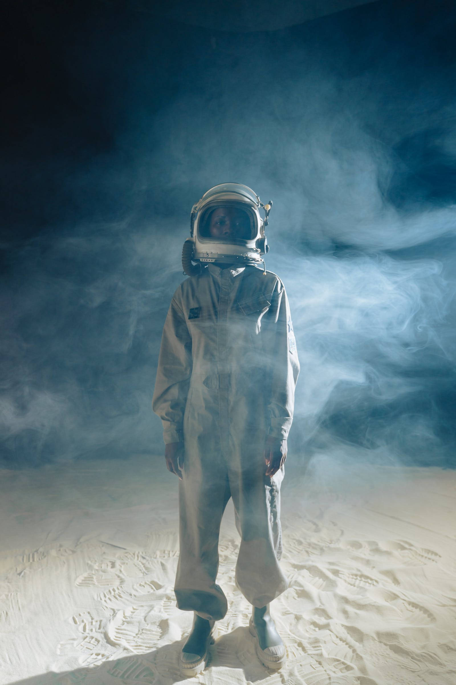 Astronaut In Space 桌布 壁紙 — 一名太空人獨自站在月球般的表面上，周圍是旋轉的藍色煙霧，天空漆黑一片。