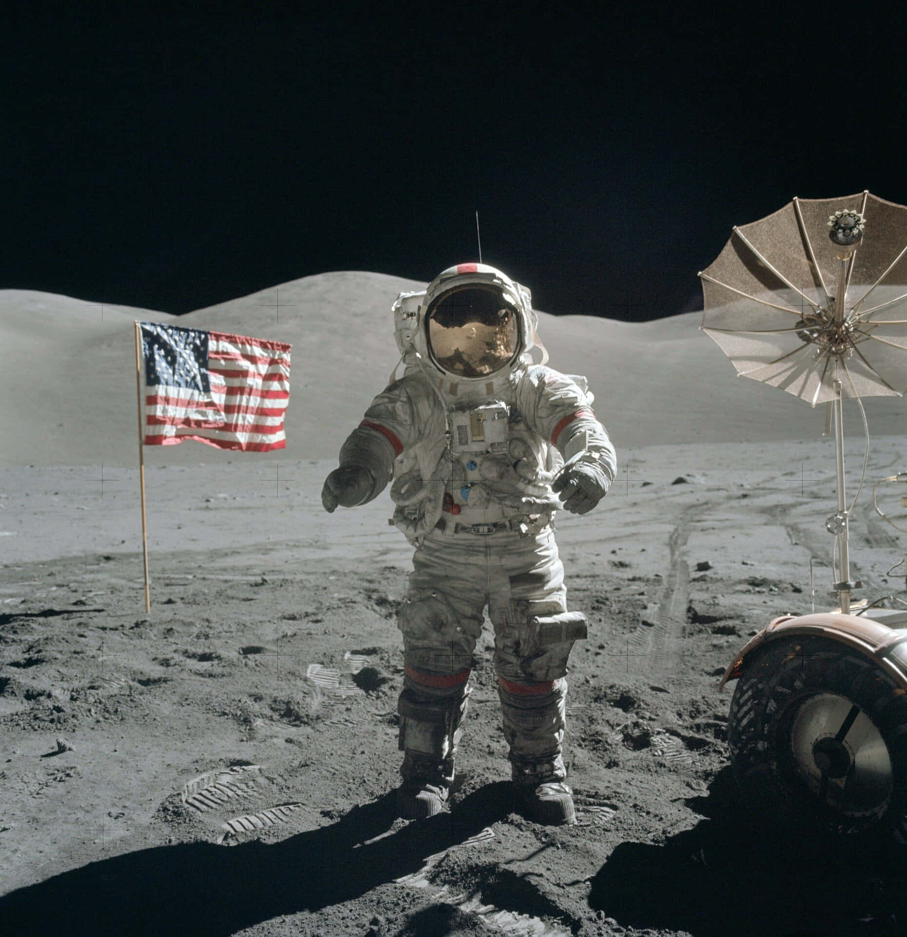 Moon Landing 桌布 壁紙 — 一名太空人站在月球灰色的表面上，旁邊是飄揚的美國國旗和月球車，背景是黑色的天空。