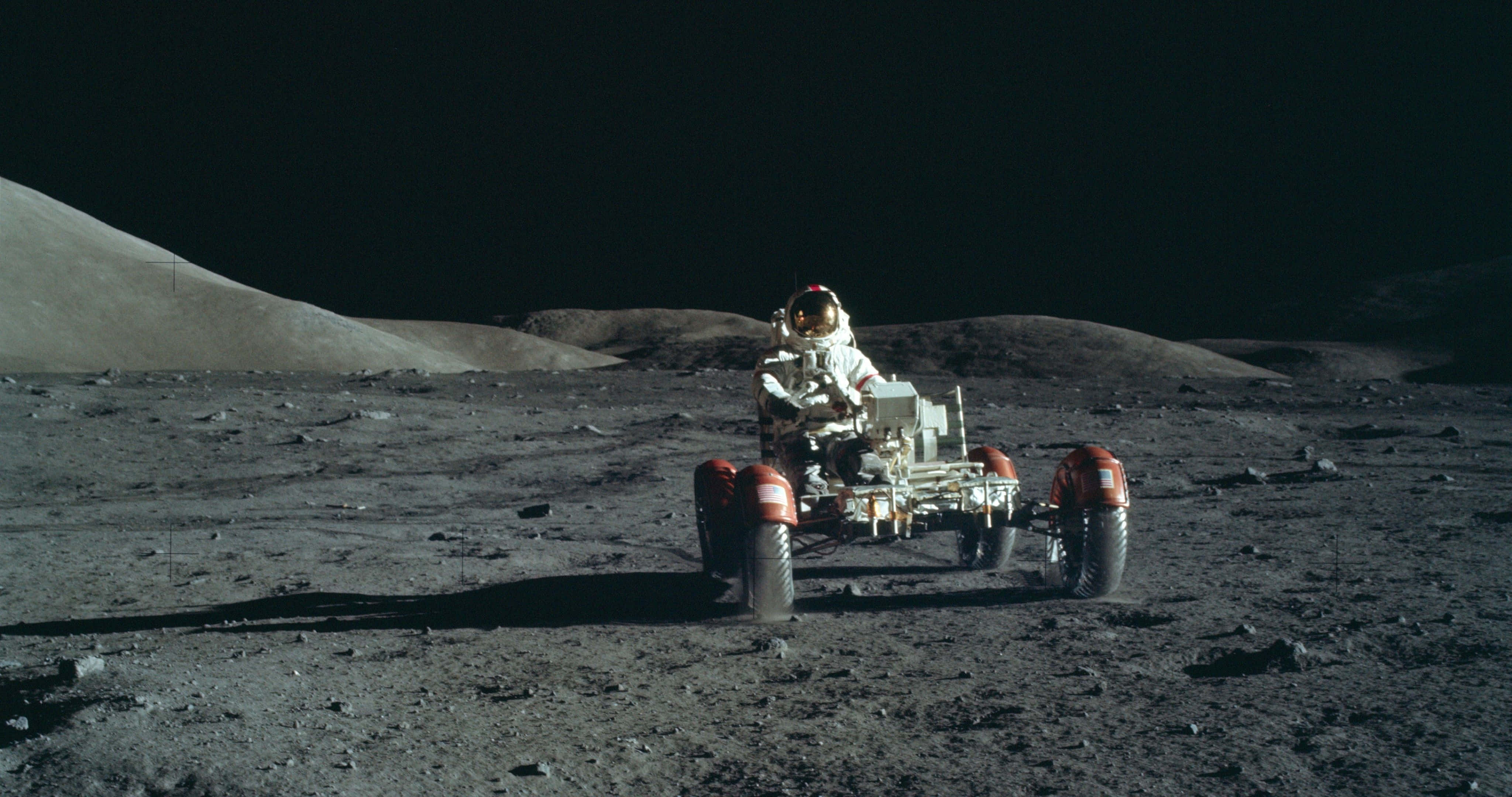 NASA 動態圖片 桌布 壁紙 — 一名太空人駕駛月球車，在黑色天空下穿越荒蕪的灰色月球表面。