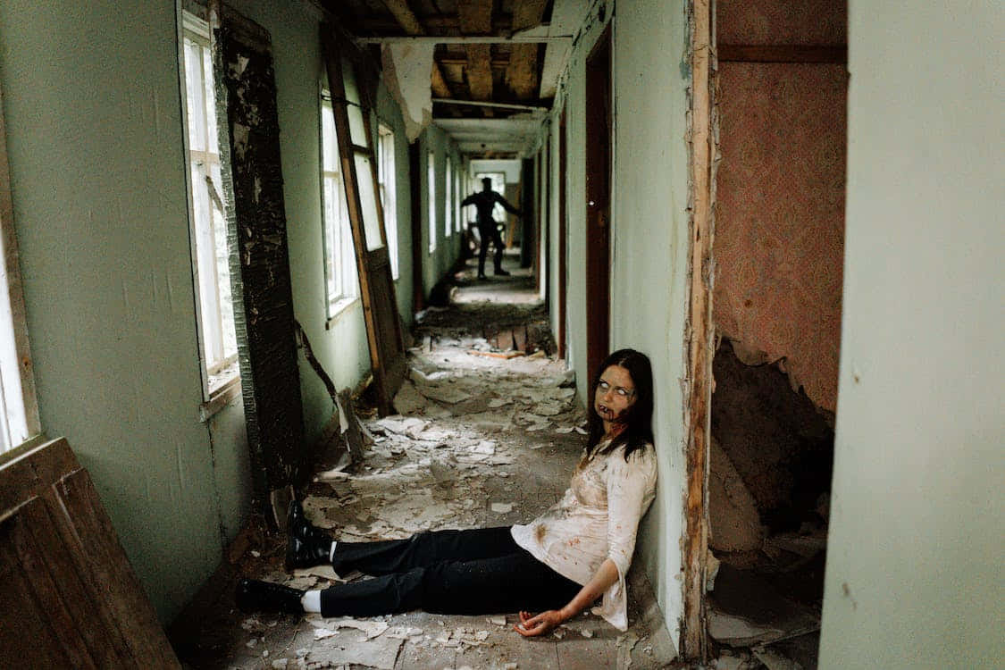 Scary Zombie 桌布 壁紙 — 一名女子受傷躺在破舊的走廊上，陰暗的身影在腐朽的走廊盡頭若隱若現。