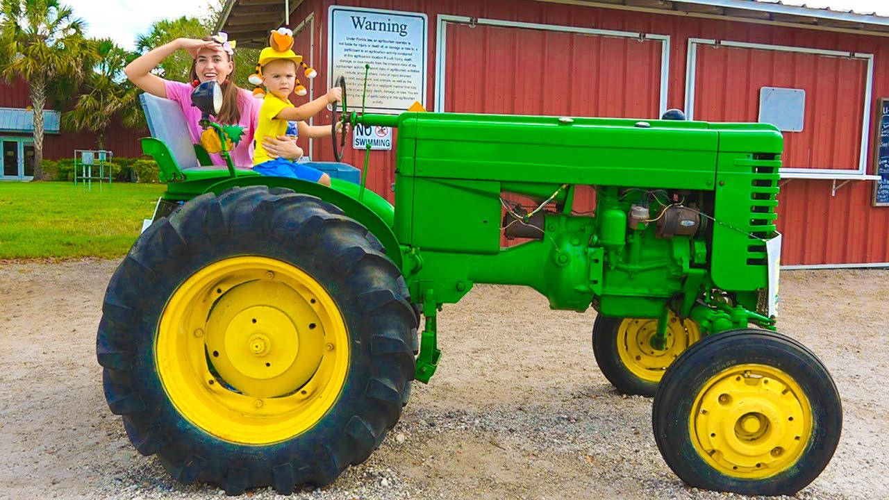 Tractor 桌布 壁紙 — 一名女子和一個孩子愉快地在一輛停在紅色穀倉前的亮綠色復古拖拉機上擺姿勢，拖拉機有黃色輪子。