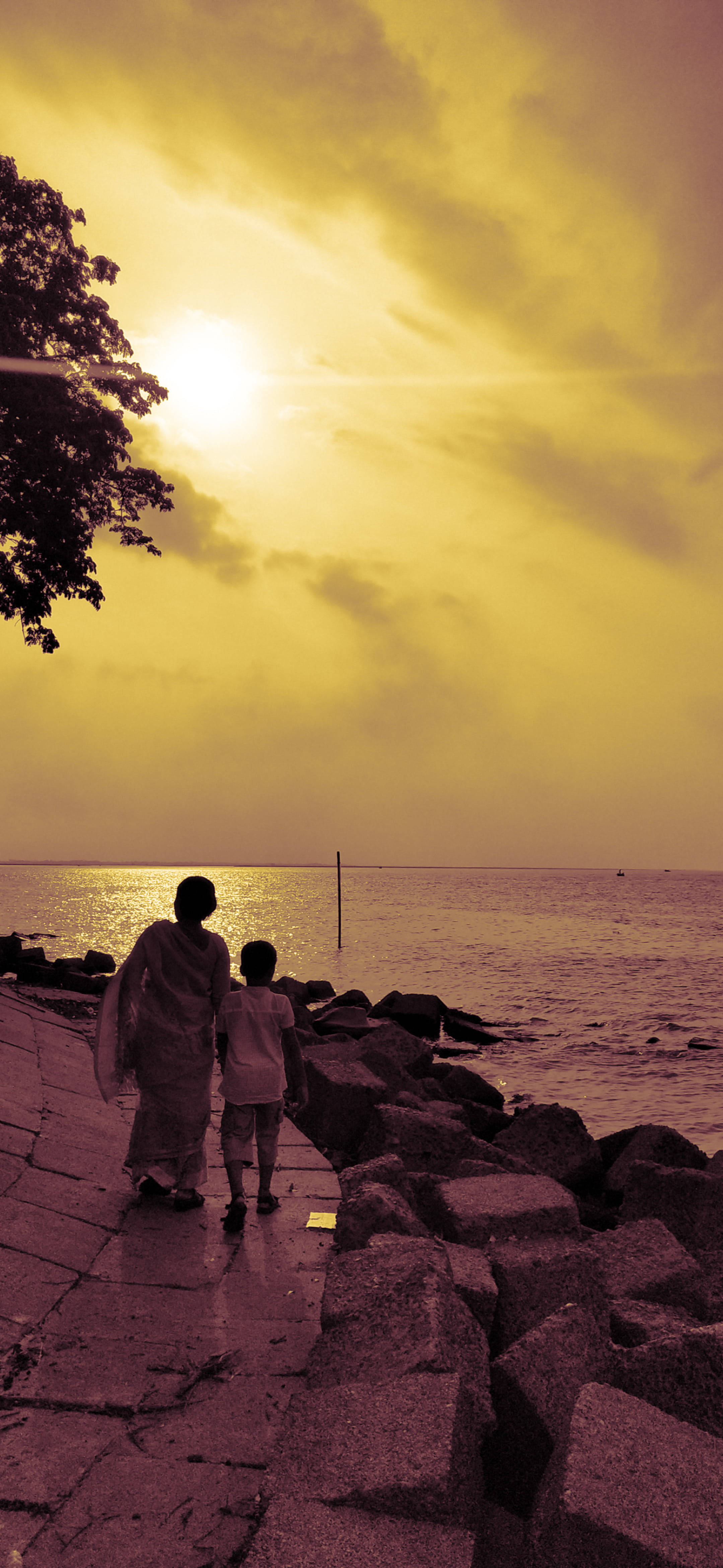 Family 桌布 壁紙 — 一名女子和一個孩子手牽手沿著石頭海堤行走，夕陽在金色薄霧中沉入海洋。