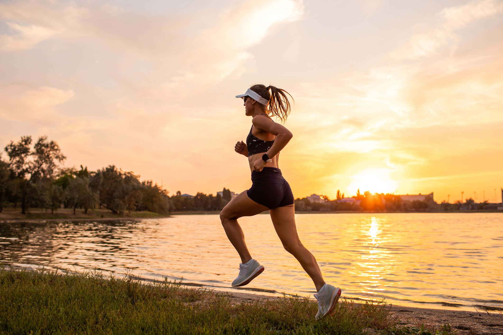 Running 桌布 壁紙 — 一名女子在日落時沿著湖岸奔跑，身後的金色光芒在水面上反射。