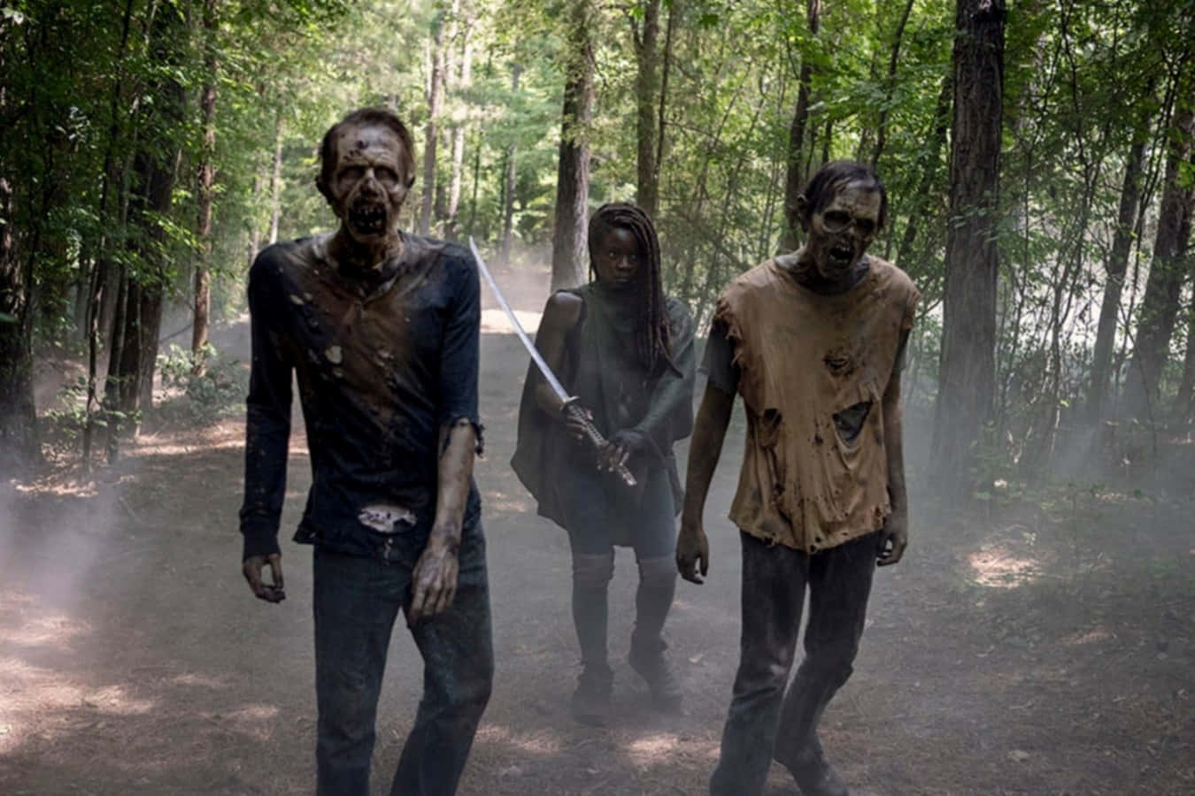 walking dead 桌布 壁紙 — 一名女子在霧氣瀰漫的森林小徑上揮劍面對兩隻腐爛的殭屍。