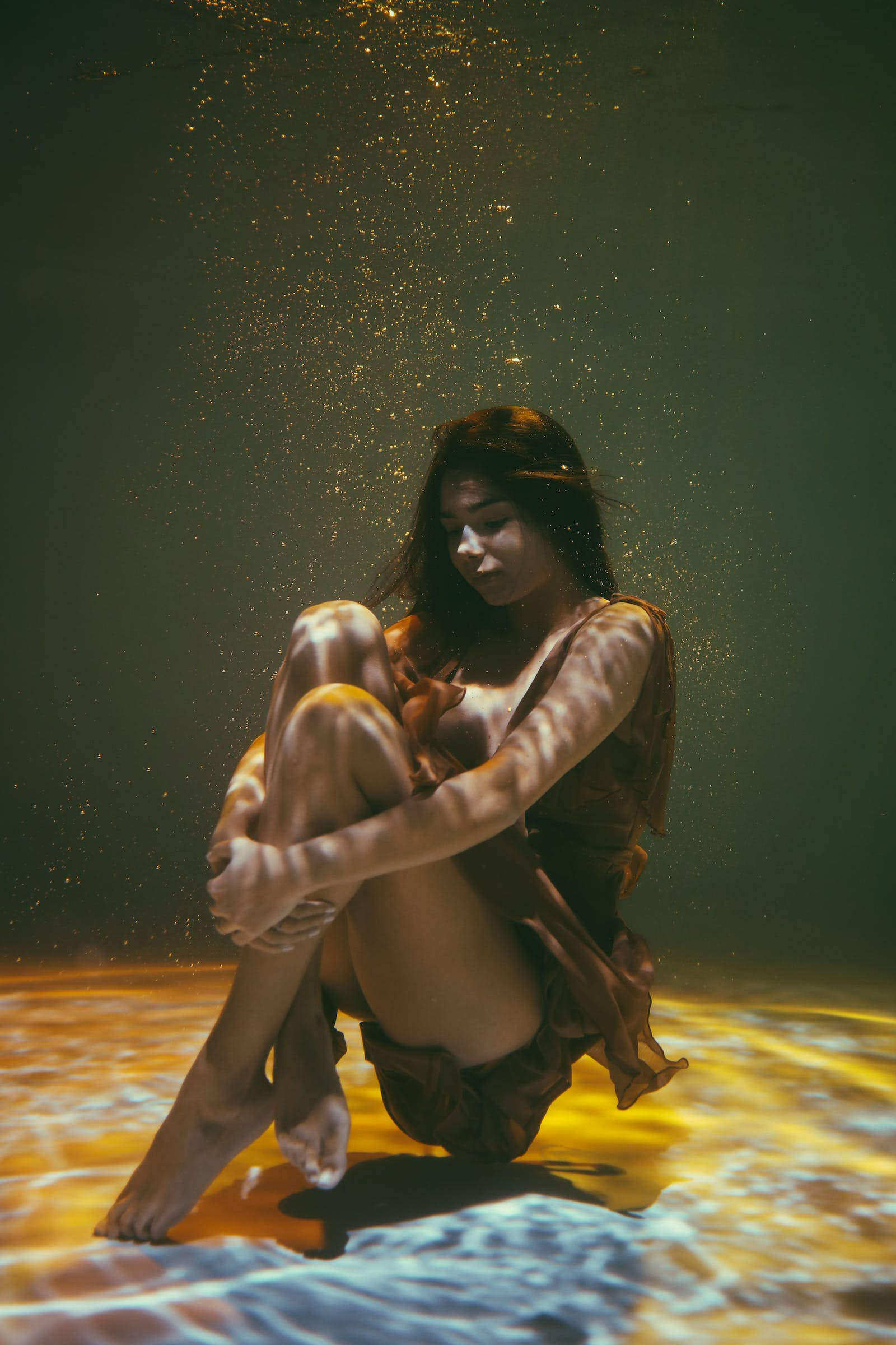 Aesthetic Photography 桌布 壁紙 — 一名女子坐在水中，金色光線穿透而過，照亮她周圍漂浮的微粒。
