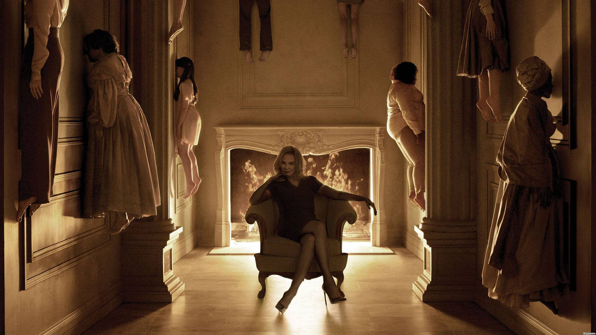 American Horror Story 桌布 壁紙 — 一名女子平靜地坐在椅子上，穿著復古連衣裙的幽靈般的身影在帶有壁爐的宏偉大廳中飄浮。