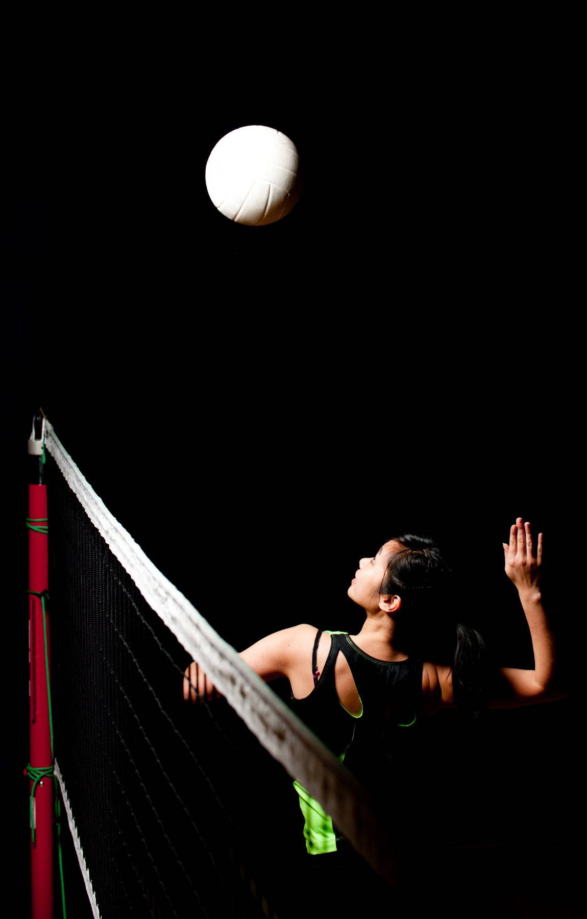 Volleyball Aesthetic 桌布 壁紙 — 一名女子排球運動員跳起扣球，背景為純黑色，帶有戲劇性的聚光燈效果。