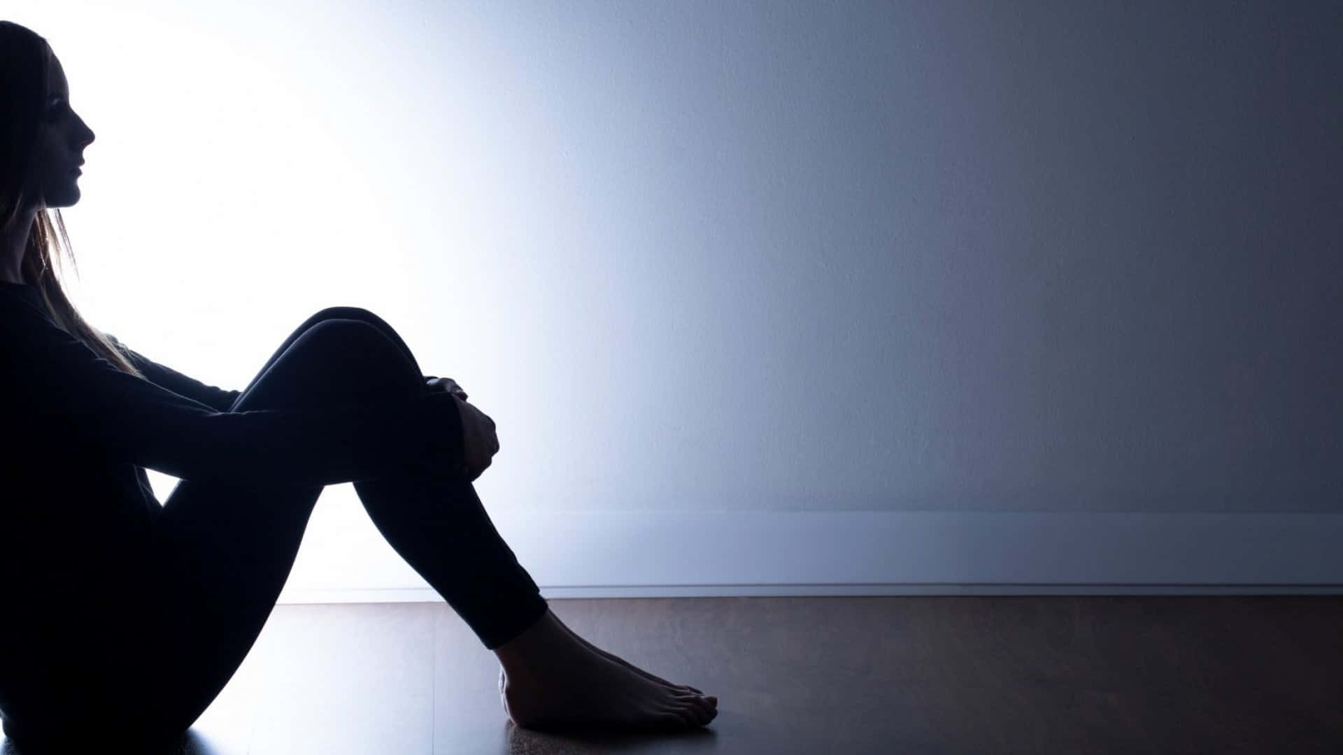 Lonely 桌布 壁紙 — 一名女子獨自坐在剪影中，背景是明亮的窗戶，柔和的光線灑在安靜房間的地板上。