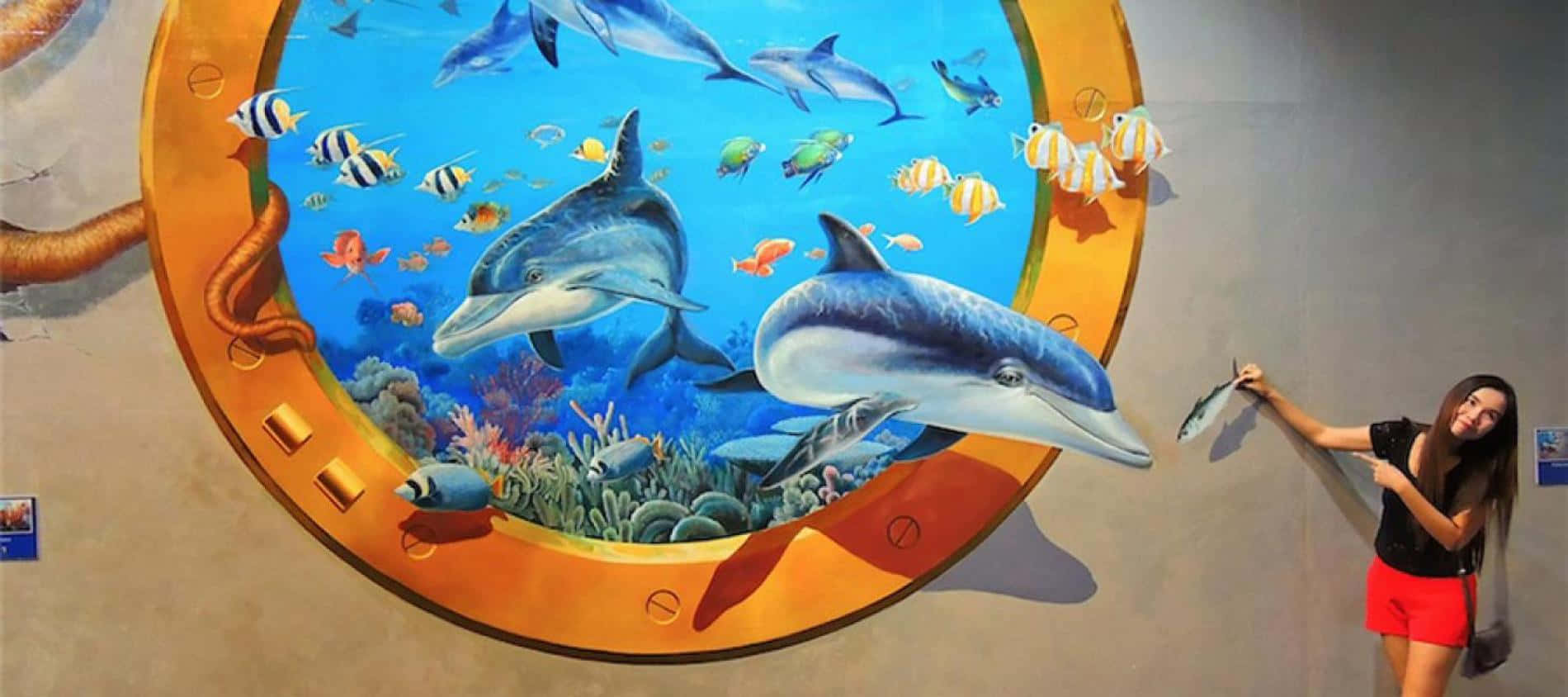 一名女子站在海豚與海洋生物壁畫旁 壁紙