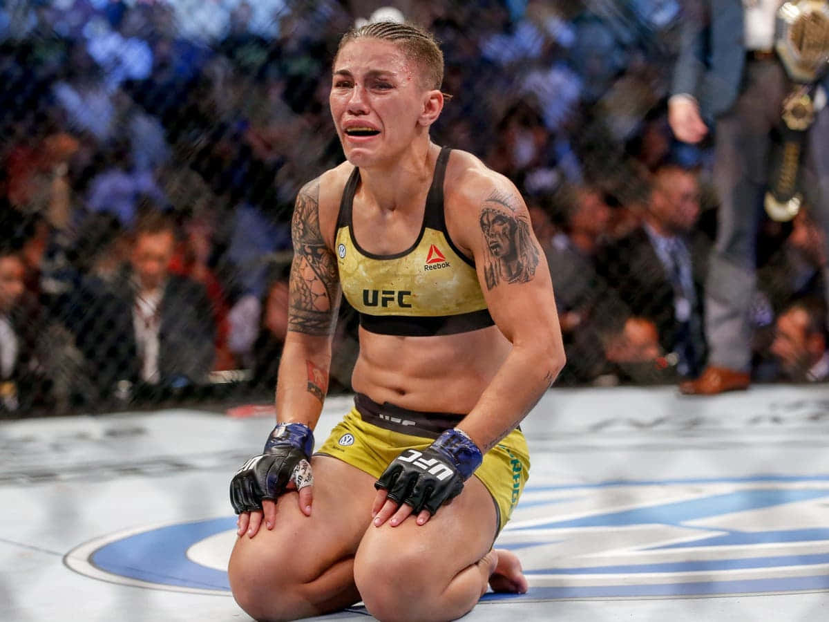 MMA 桌布 壁紙 — 一名女性MMA拳手在比賽後跪在八角籠地上，情緒激動流淚，背景有觀眾。