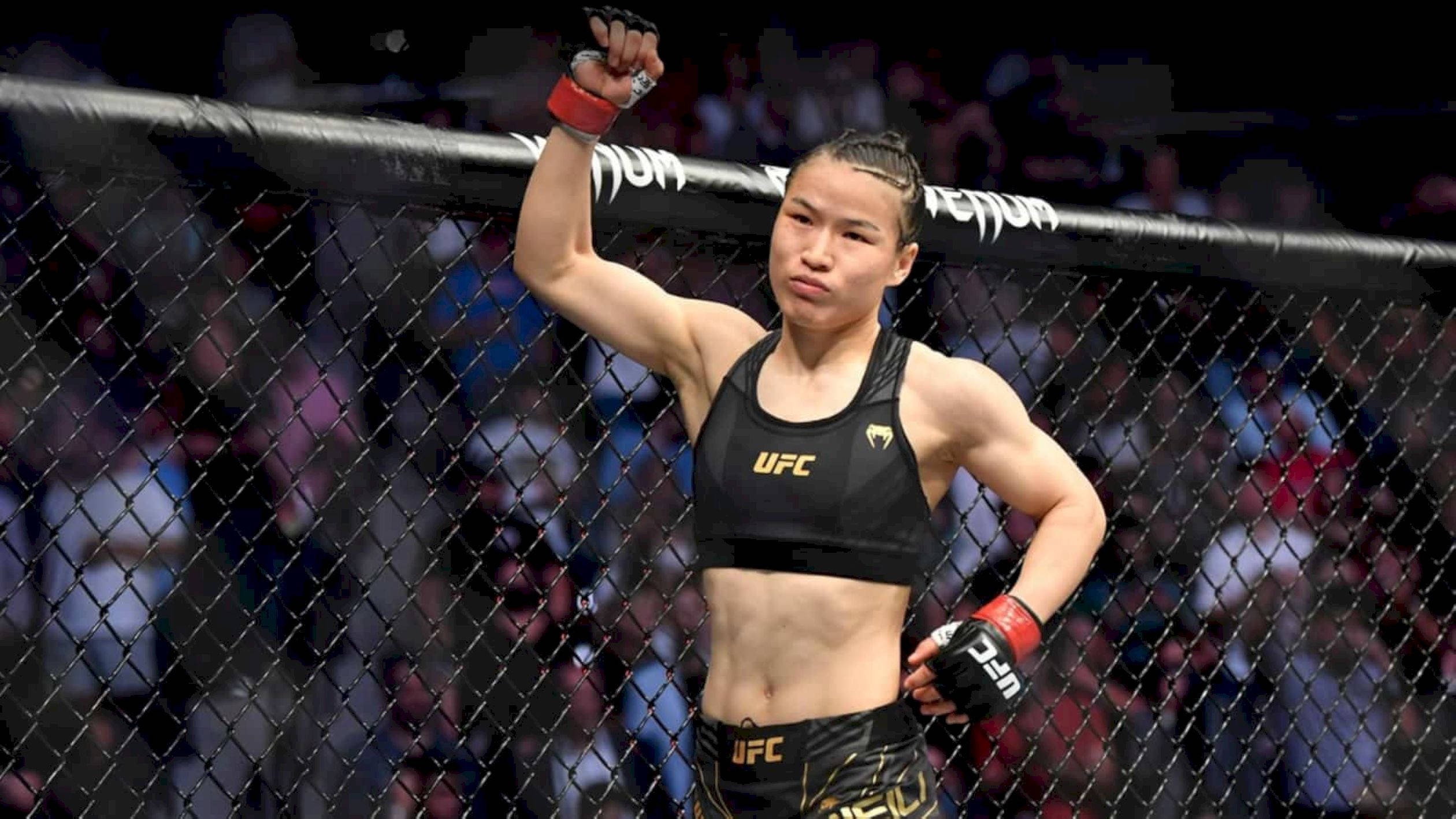 Champion 桌布 壁紙 — 一名女性UFC拳手在八角籠內高舉拳頭慶祝勝利，鐵絲網後面是模糊的人群。