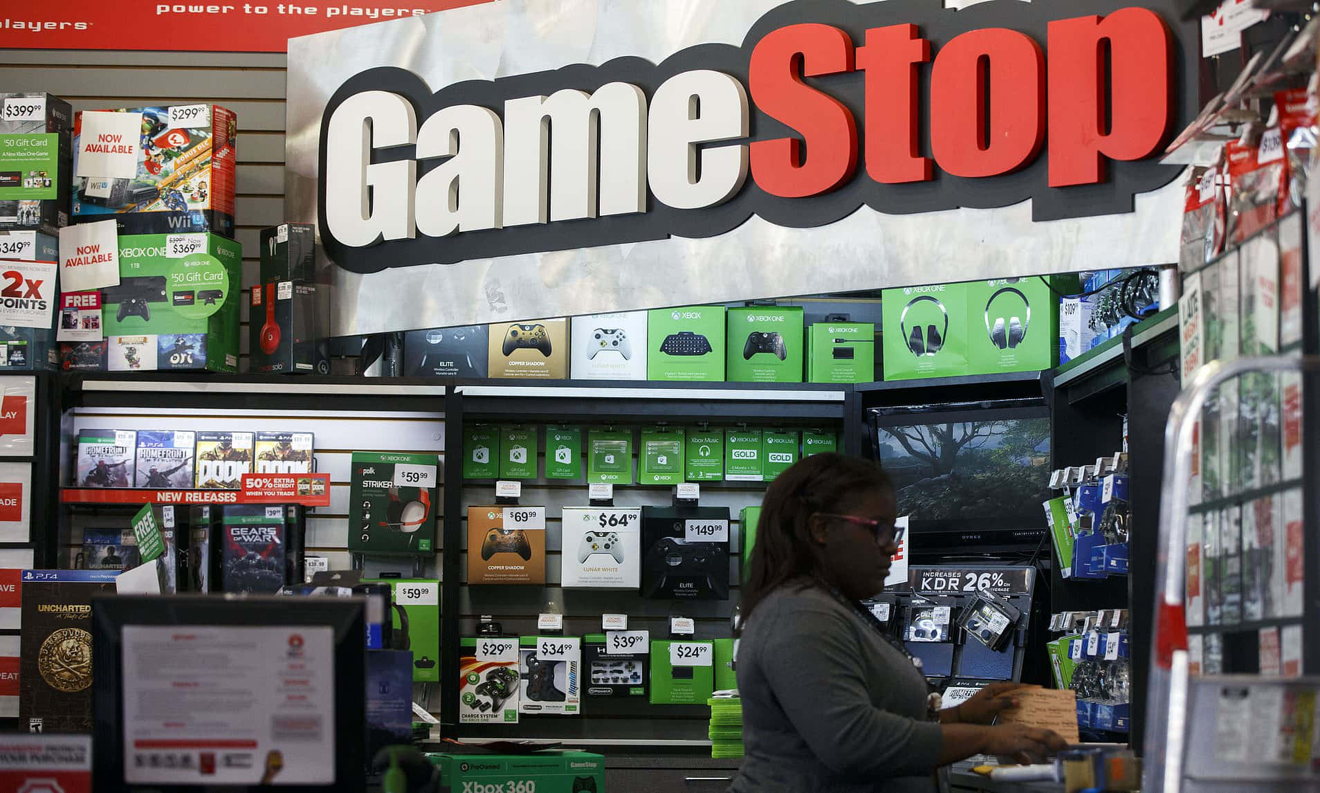 GameStop 桌布 壁紙 — 一名女性在GameStop零售店內明亮的店舖燈光下瀏覽電子遊戲商品。