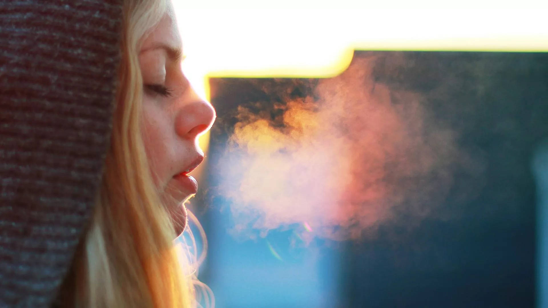 呼吸 桌布 壁紙 — 一名女性在溫暖的日落餘暉中呼出一團蒸氣，柔和的金色光線勾勒出她的側面輪廓。