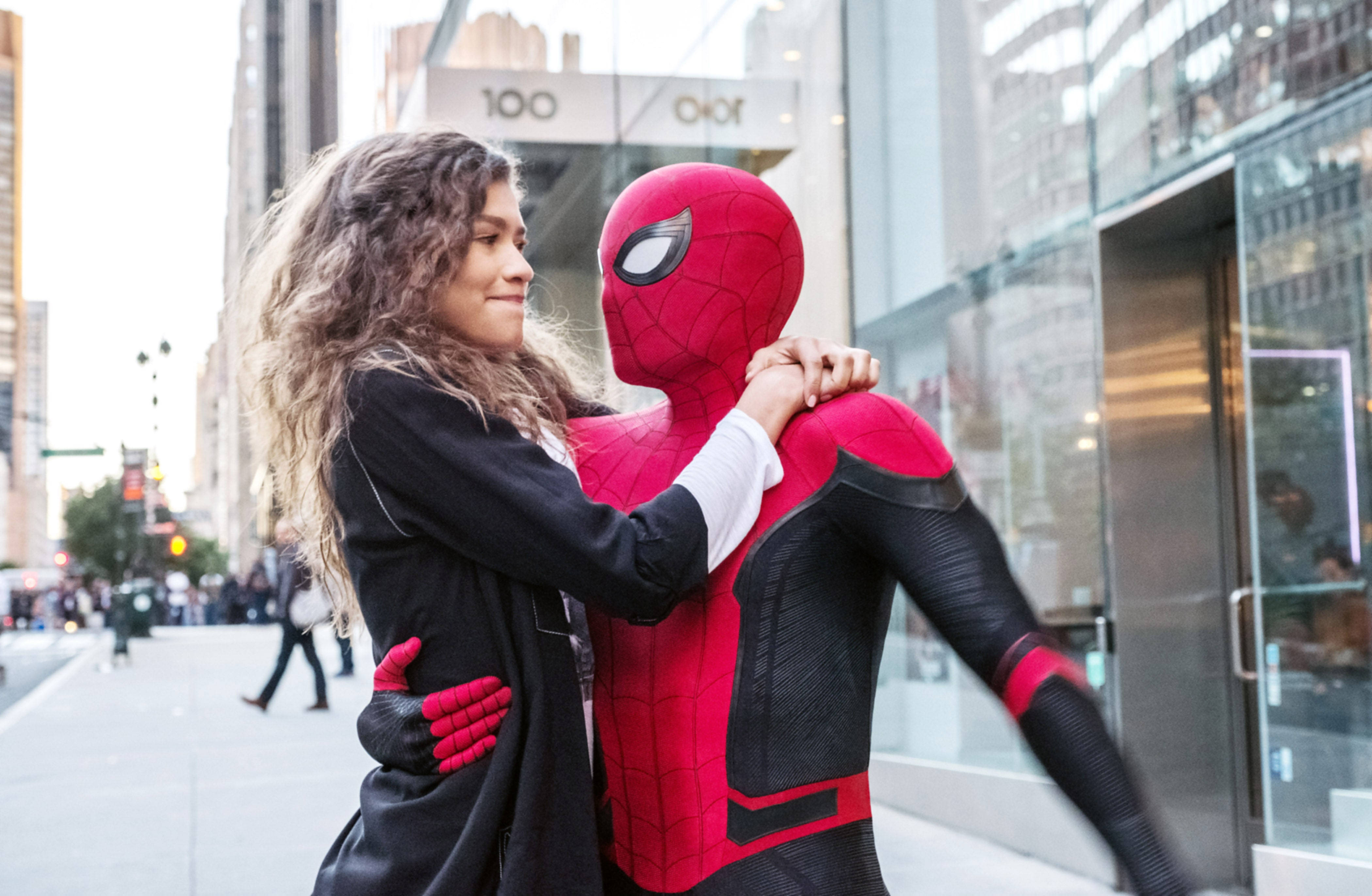 Zendaya 桌布 壁紙 — 一名女性在繁忙的城市人行道上擁抱一個穿著紅黑色蜘蛛人服裝的人。