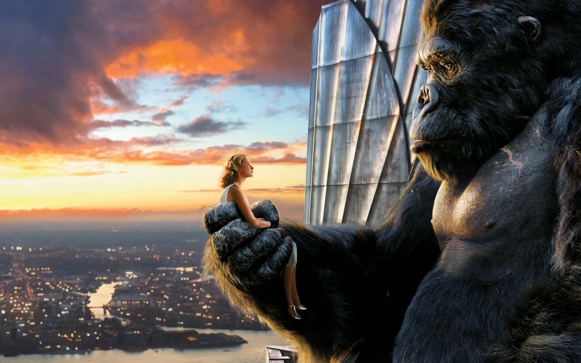 King Kong 桌布 壁紙 — 一名女性平靜地坐在巨型大猩猩的手掌中，俯瞰夕陽下火橙色雲朵籠罩的廣闊城市。