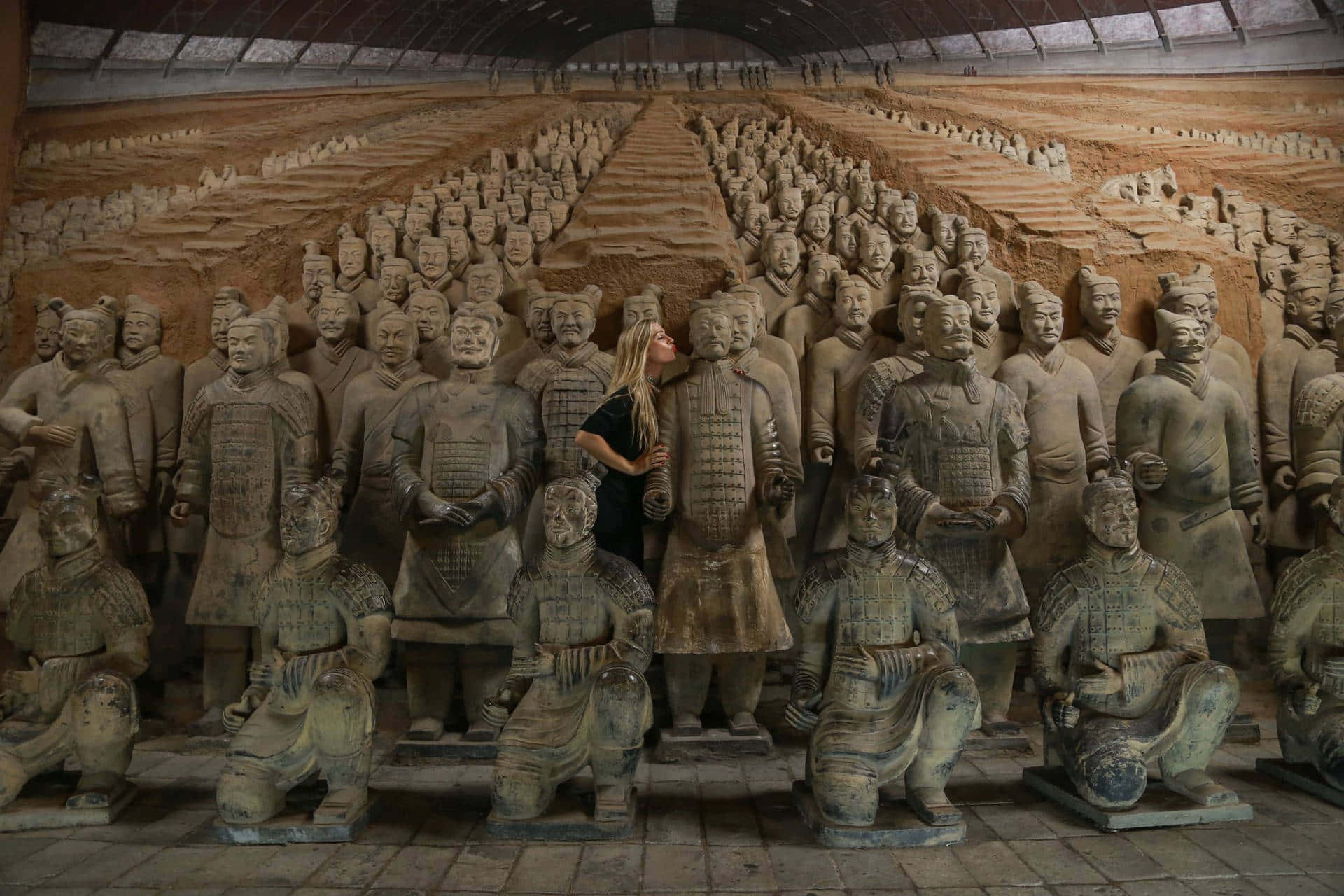 Museum 桌布 壁紙 — 一名女性站在保護屋頂下的發掘坑中，置身於一排排古代兵馬俑之間。