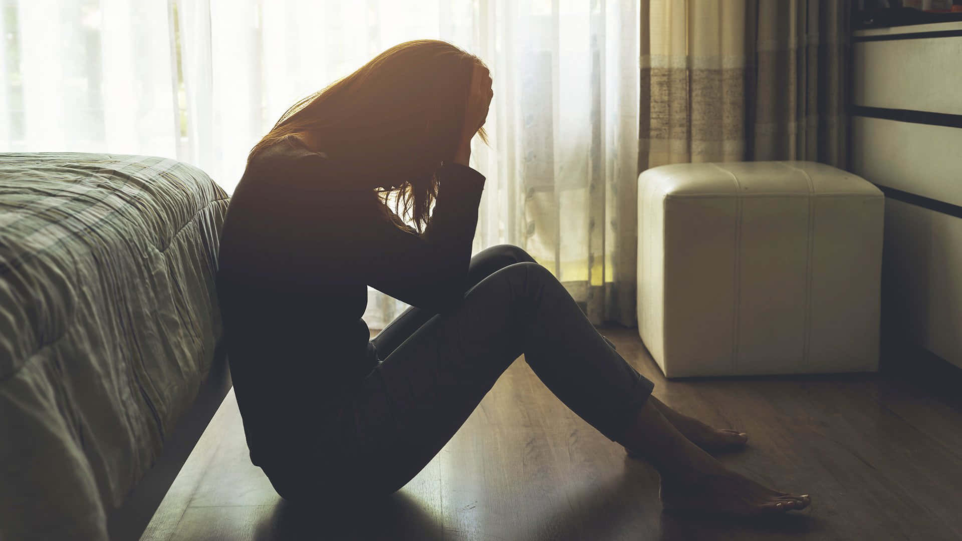 Depressed 桌布 壁紙 — 一名女性蜷縮坐在床邊的木地板上，被柔和窗光映成剪影，雙手抱頭，陷入靜默的痛苦。