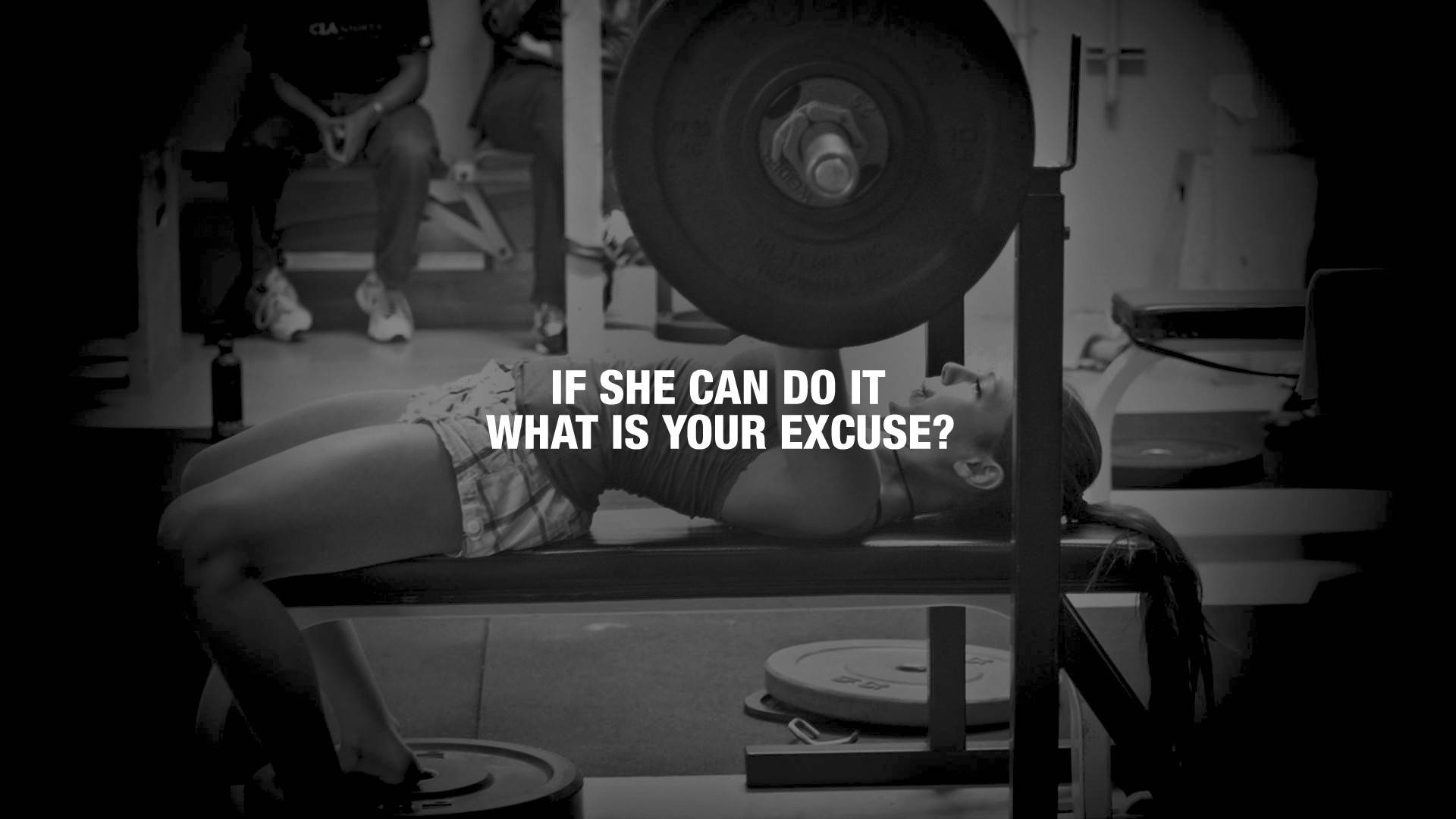 Motivation 桌布 壁紙 — 一名女性躺在臥推架上，在燈光昏暗的健身房中舉起沉重的槓鈴，並疊加了激勵文字。