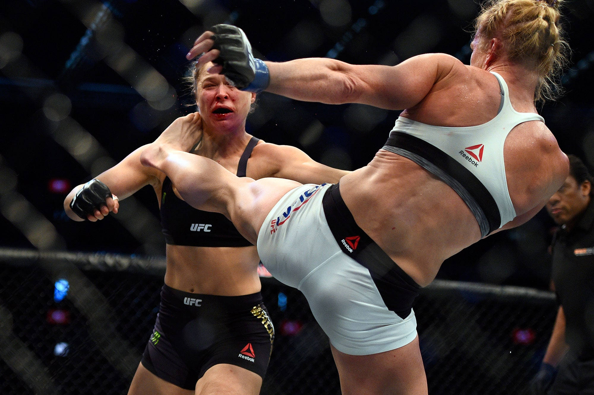 Rousey 桌布 壁紙 — 一名女拳手在燈光明亮的UFC八角籠中向對手使出強力高踢。