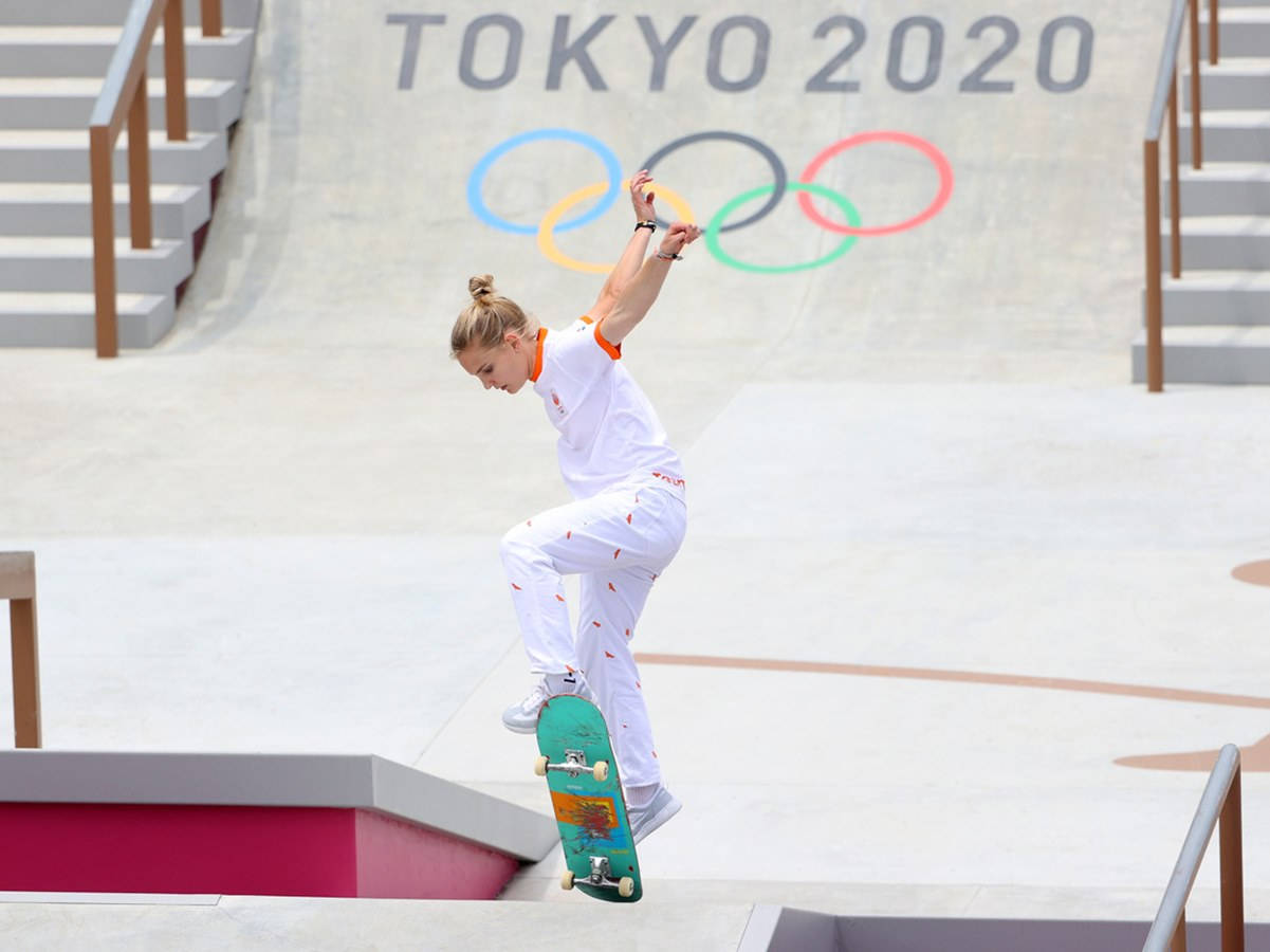 Olympics 桌布 壁紙 — 一名女滑板選手在東京2020奧運會滑板公園中凌空表演技巧，背景有奧運五環。