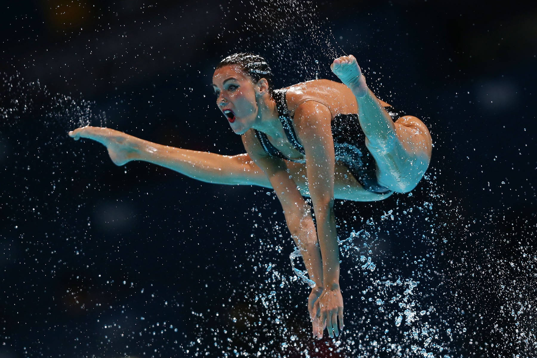 Olympics 桌布 壁紙 — 一名女潛水員在黑暗背景前以動態姿勢被捕捉到空中，水滴在她周圍飛舞。