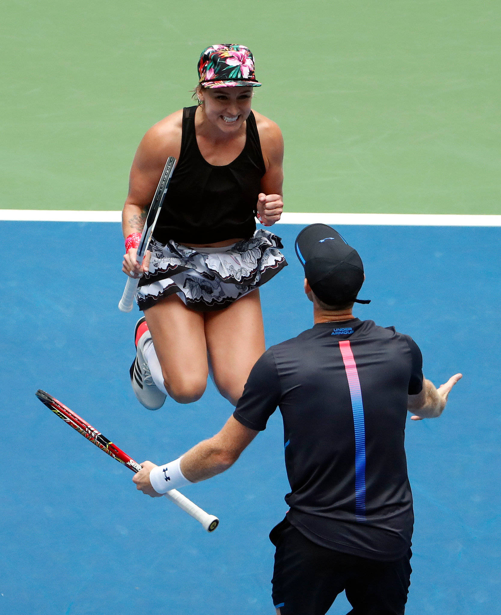 Tennis 桌布 壁紙 — 一名女網球運動員在藍色球場上歡快地躍起，而一名男運動員則向她做手勢。