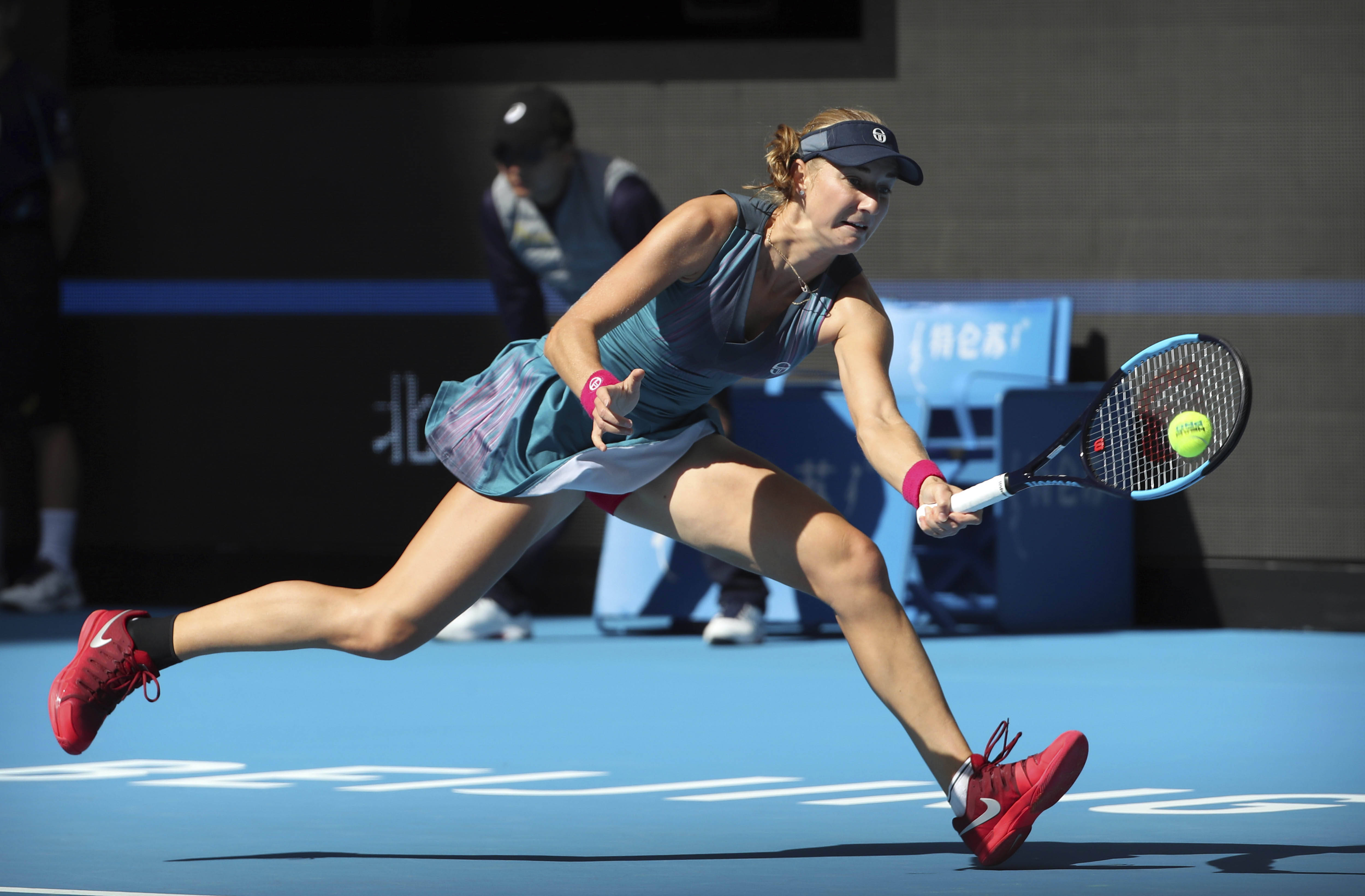 Athletic 桌布 壁紙 — 一名女網球選手在藍色球場上向前撲出，在明亮的日光下以高度專注擊打黃色球。