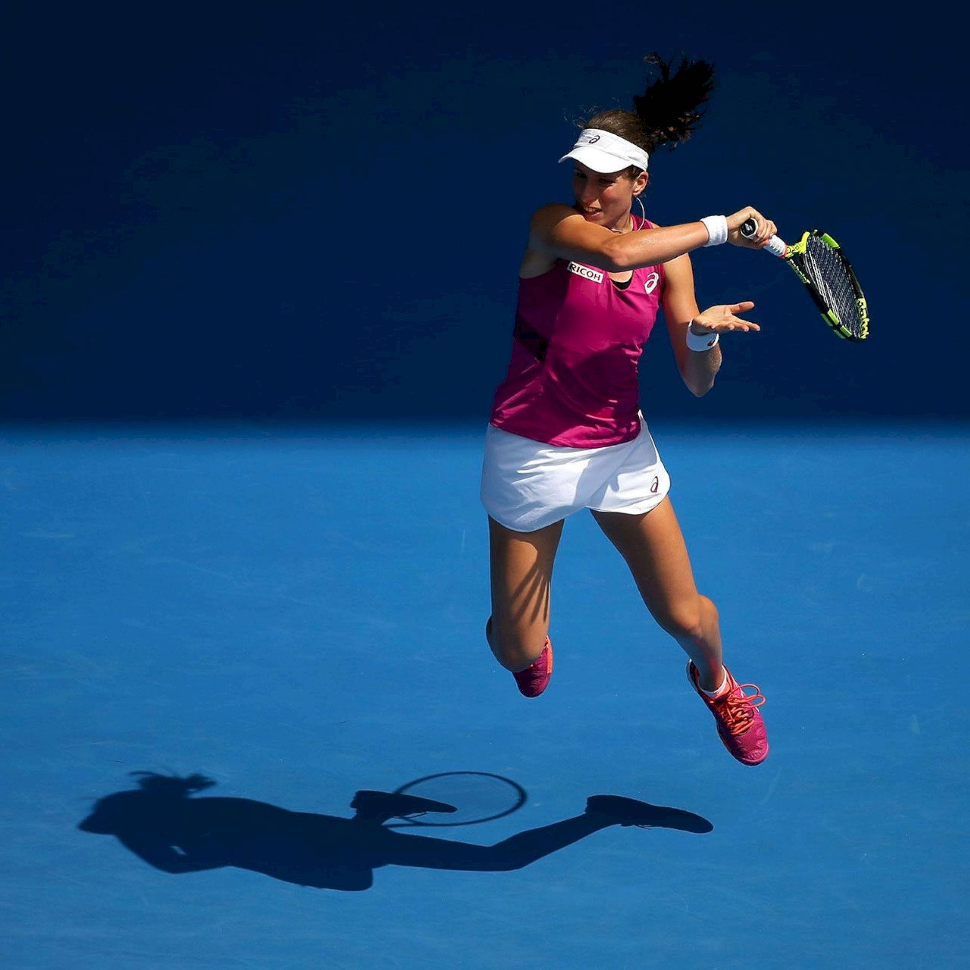 Athletic 桌布 壁紙 — 一名女網球選手在藍色球場上躍起，以動態動作揮動球拍。