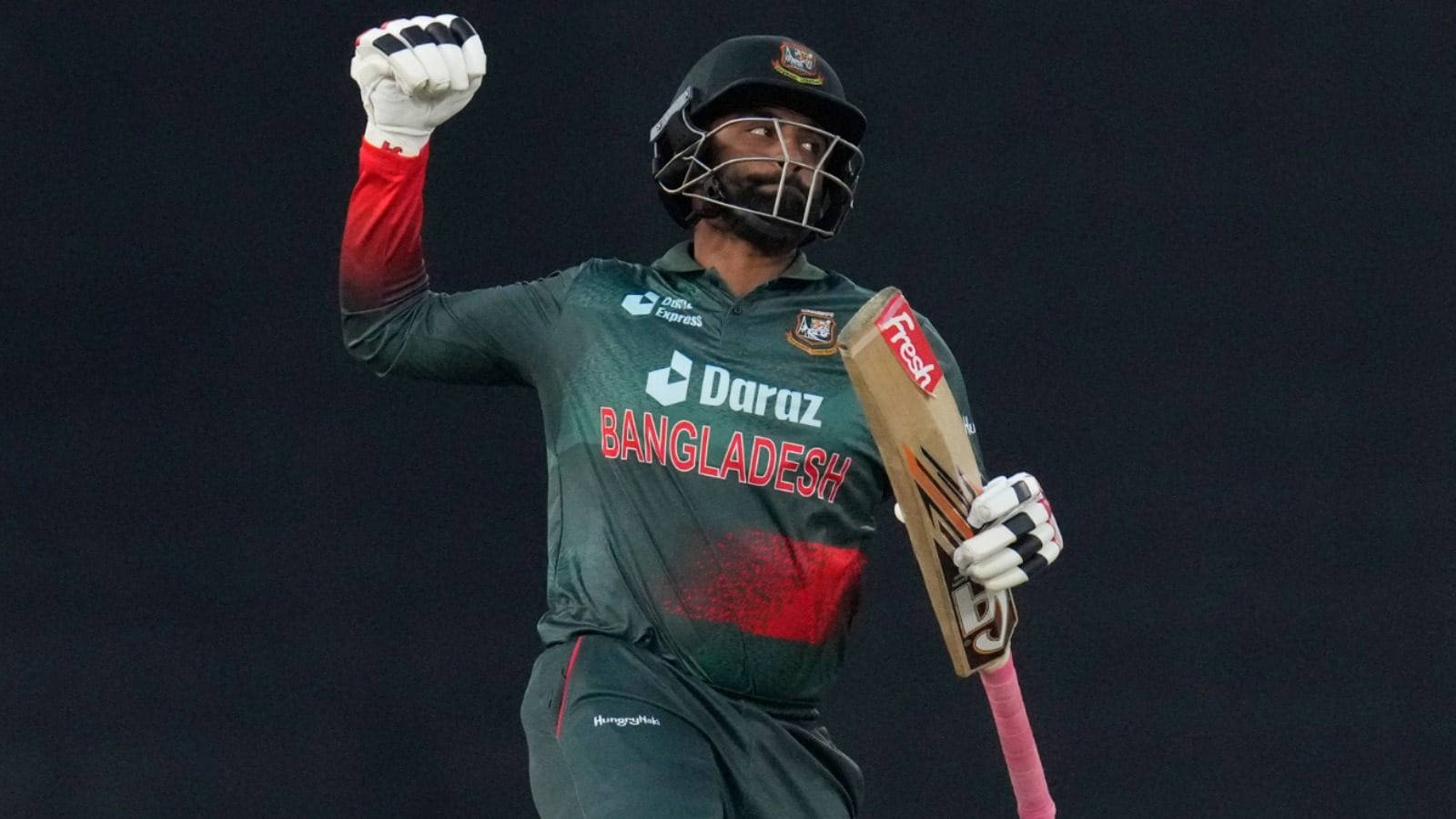 Bangladesh Cricket 桌布 壁紙 — 一名孟加拉國板球運動員身穿綠色和紅色制服，在深色背景下高舉拳頭，勝利地握著球棒。