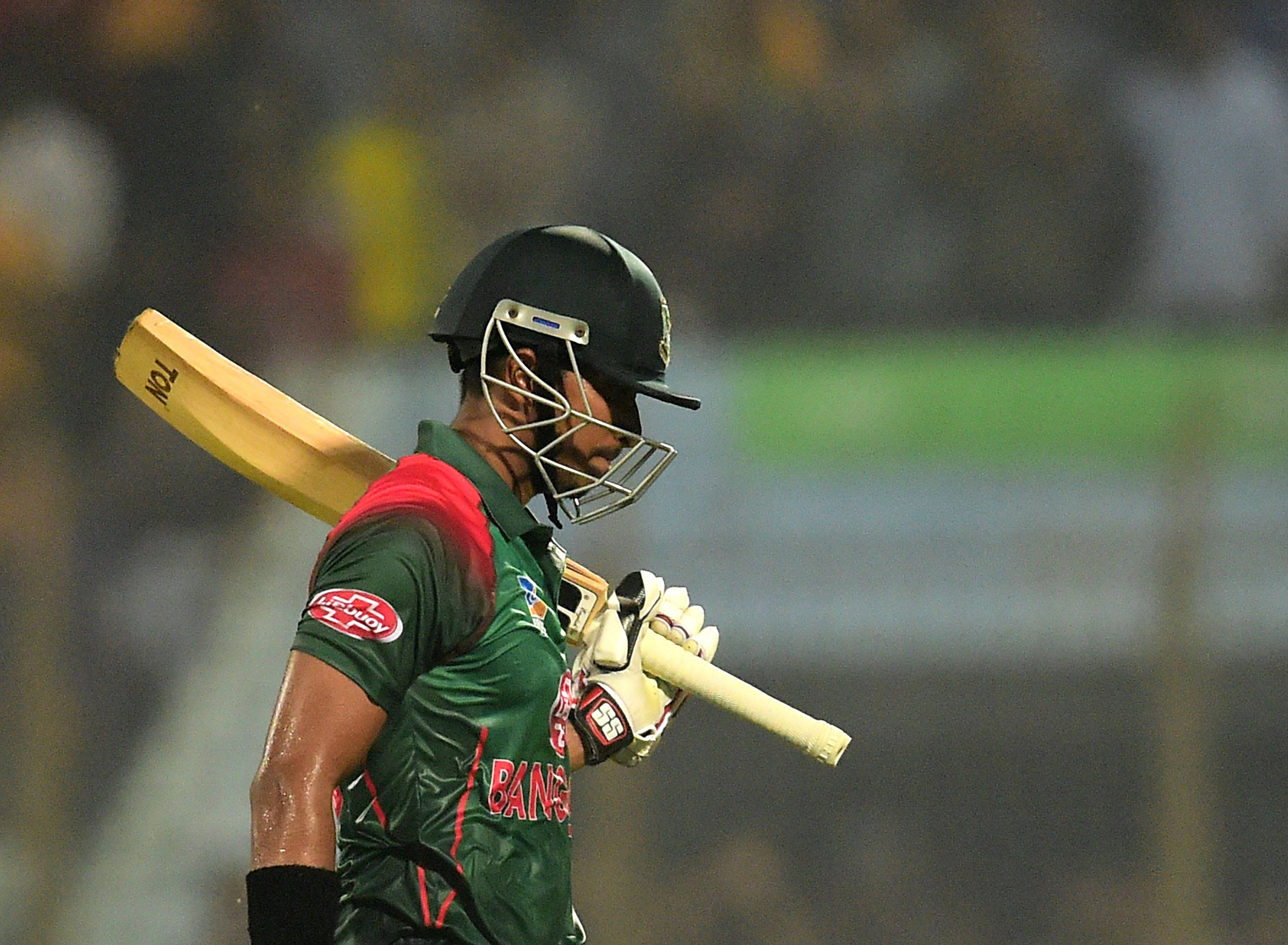 Bangladesh Cricket 桌布 壁紙 — 一名孟加拉板球運動員身穿綠色和紅色制服，在夜間比賽中，在體育場燈光下將球棒扛在肩上。