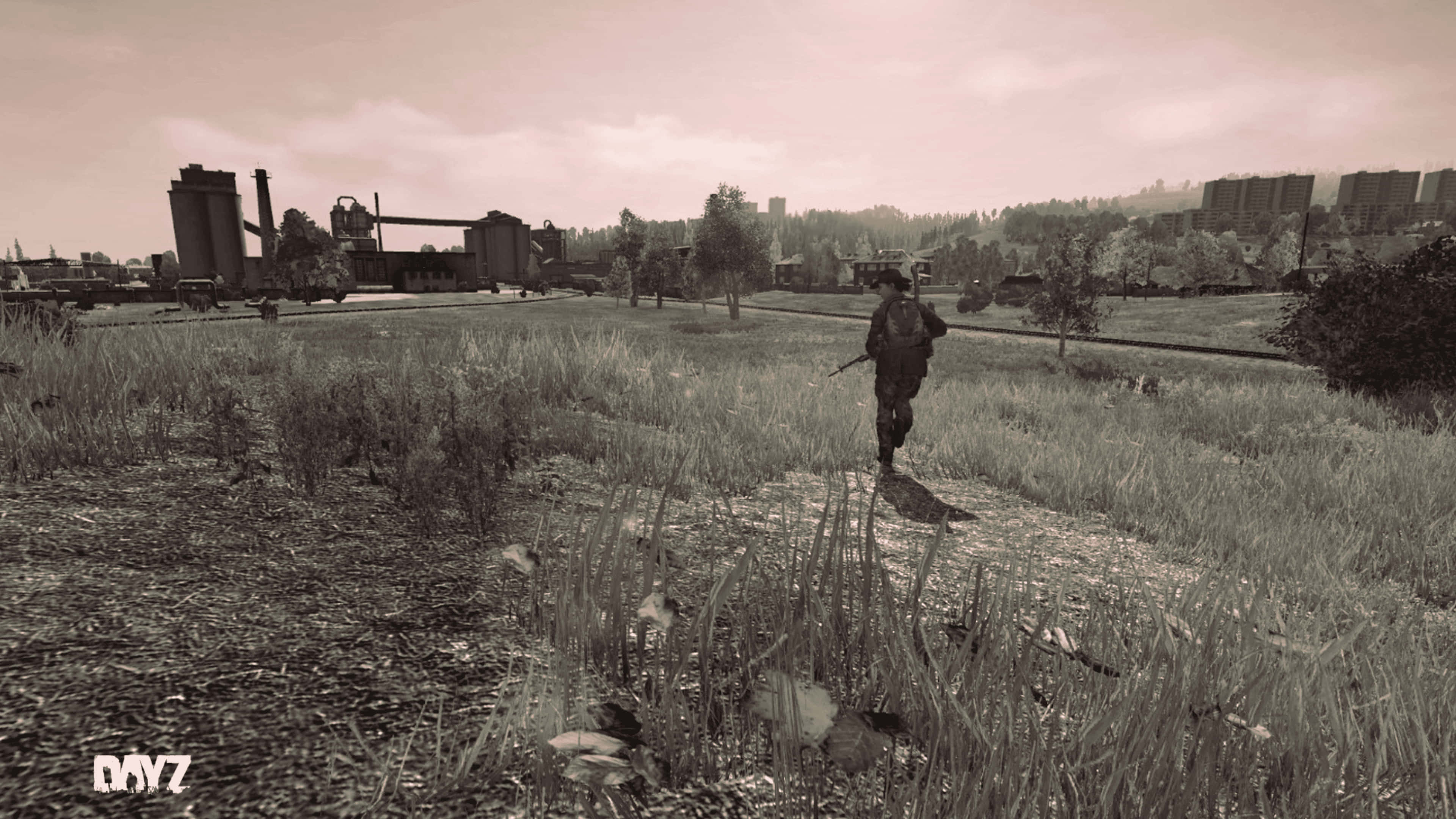 Dayz Mod 桌布 壁紙 — 一名孤獨的士兵穿過雜草叢生的草地，走向遠處的工業建築，天空朦朧。