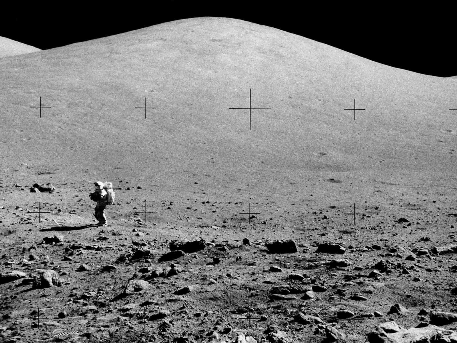 Moon Landing 桌布 壁紙 — 一名孤獨的太空人在漆黑的天空下，走過荒蕪多石的月球表面，遠方有柔和的山丘。