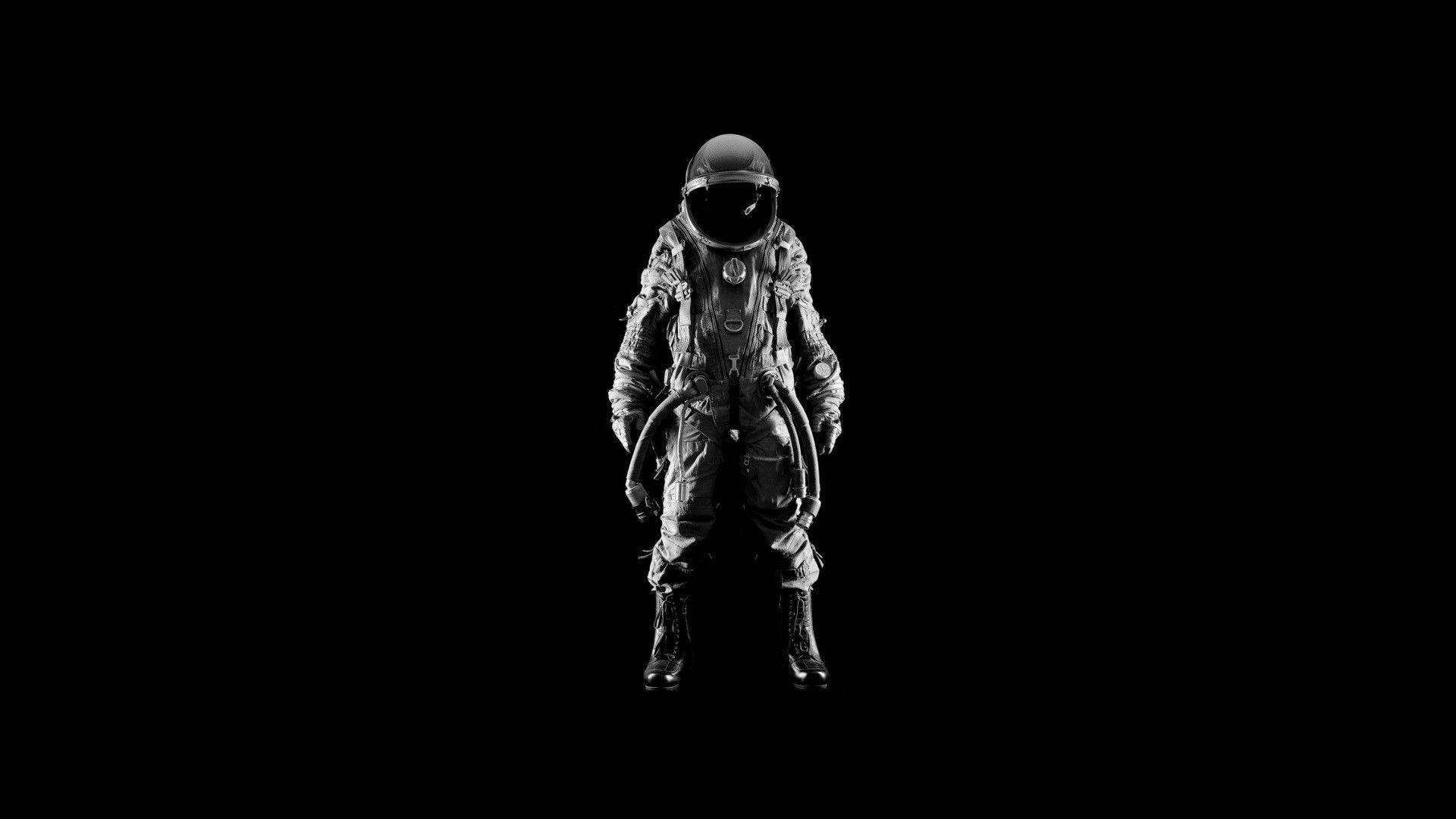astronaut aesthetic 桌布 壁紙 — 一名孤獨的太空人穿著細節豐富的太空衣，站在純黑色的虛空中，頭盔沒有反射任何東西。
