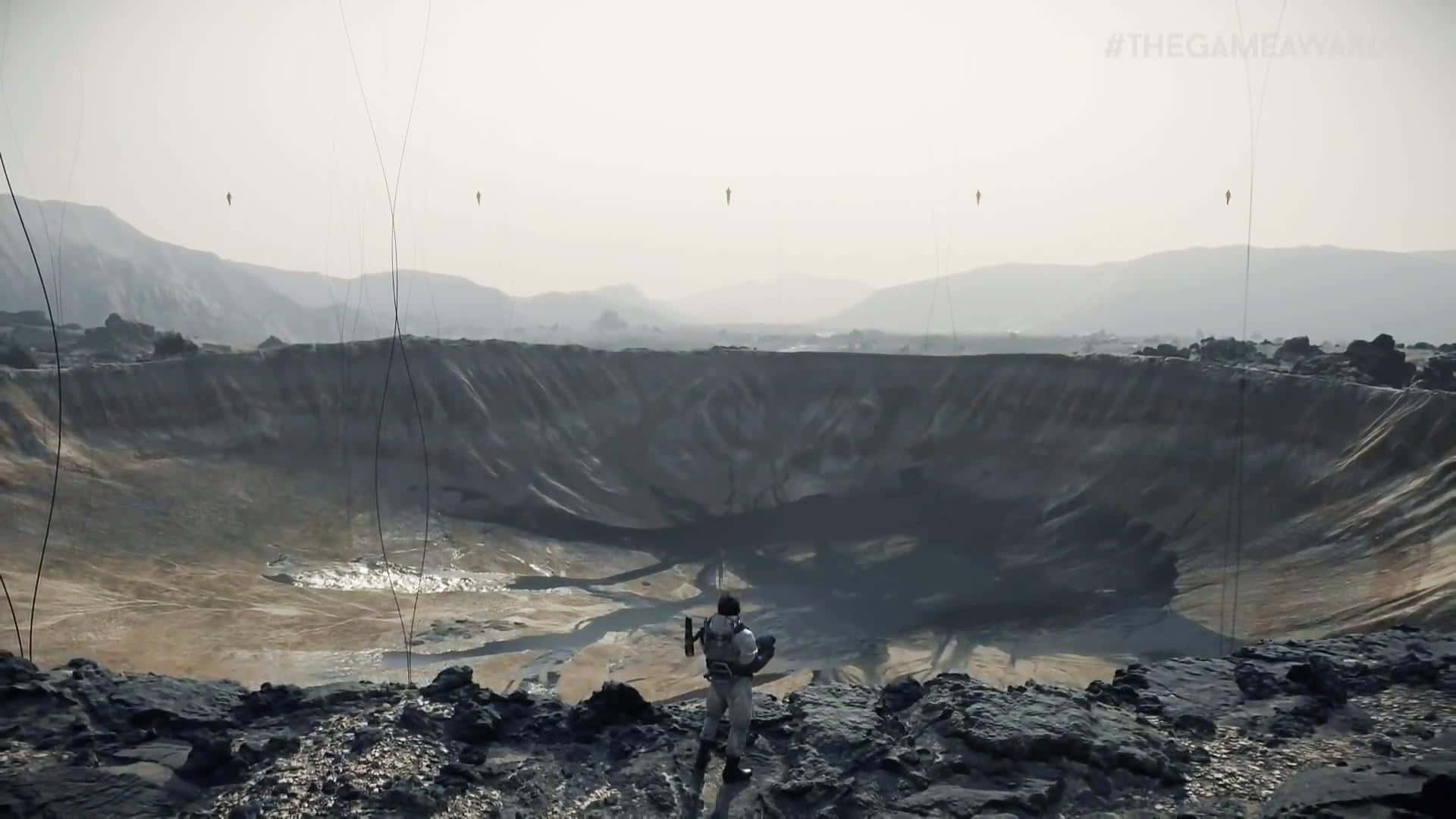 Death Stranding Pc 桌布 壁紙 — 一名孤獨的太空人站在岩石嶙峋的隕石坑邊緣，俯瞰著朦朧天空下廣闊荒涼的外星地貌。