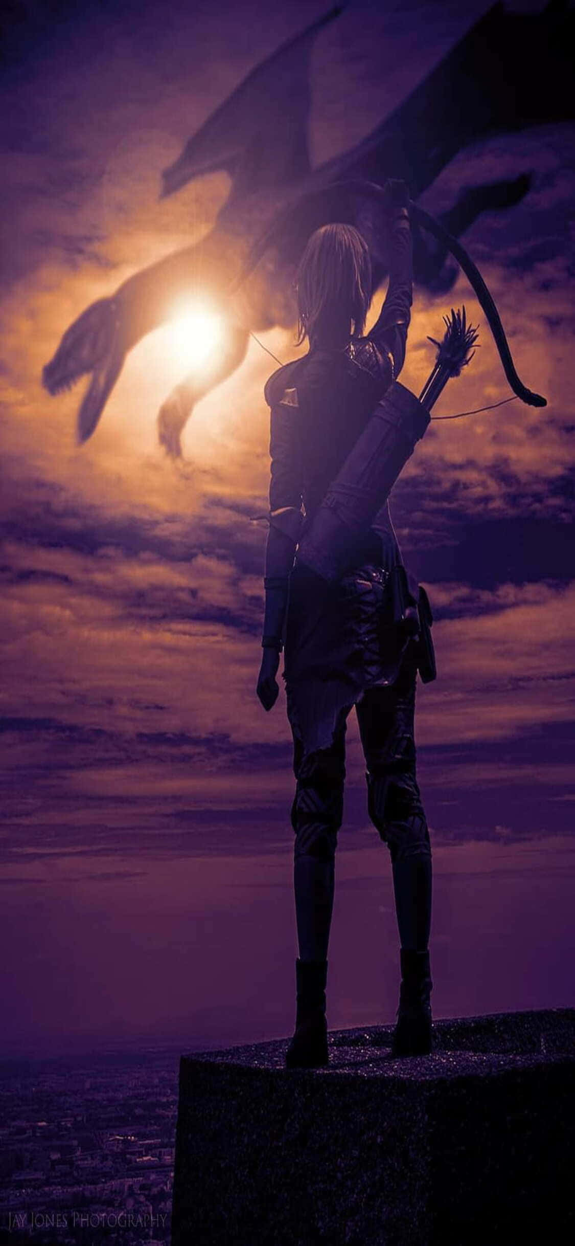 iPhone Xs Dragon Age Inquisition 桌布 壁紙 — 一名孤獨的弓箭手站在懸崖上，在夕陽下瞄準發光天空中巨龍的剪影。