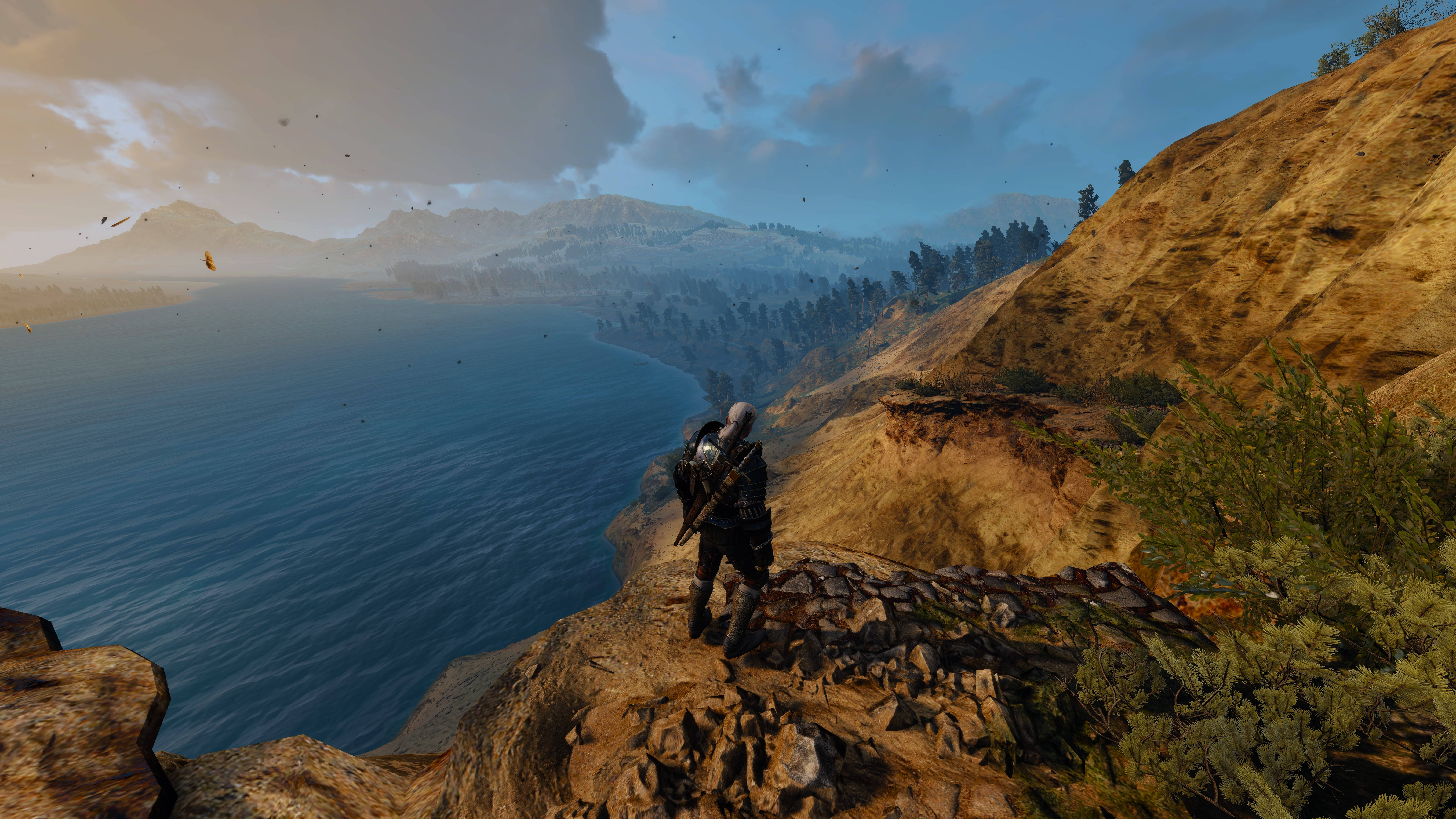 witcher 4K 桌布 壁紙 — 一名孤獨的戰士站在岩石峭壁上，俯瞰著廣闊的藍色海洋和遠山，天空多雲。