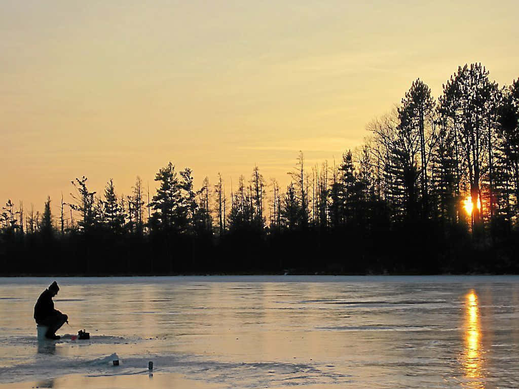 Ice Fishing 桌布 壁紙 — 一名孤獨的漁夫在日落時分坐在結冰的湖面上，金色的光線在冰面上反射，投下長長的影子。