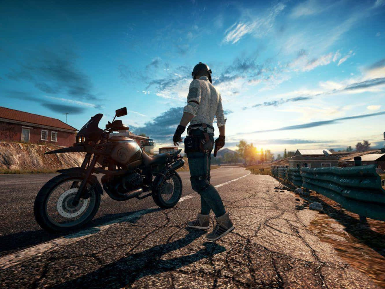 Playerunknowns Battleground Desktop 桌布 壁紙 — 一名孤獨的騎士戴著頭盔和裝備，在日落時分沿著一條裂開的道路行走，旁邊是一輛堅固的摩托車，遠處有一個小村莊。