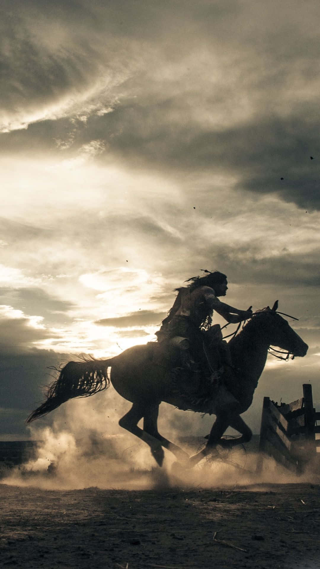 Western Cowboy iPhone 桌布 壁紙 — 一名孤獨的騎手騎著奔騰的馬，在戲劇性的金色日落天空下揚起塵土。