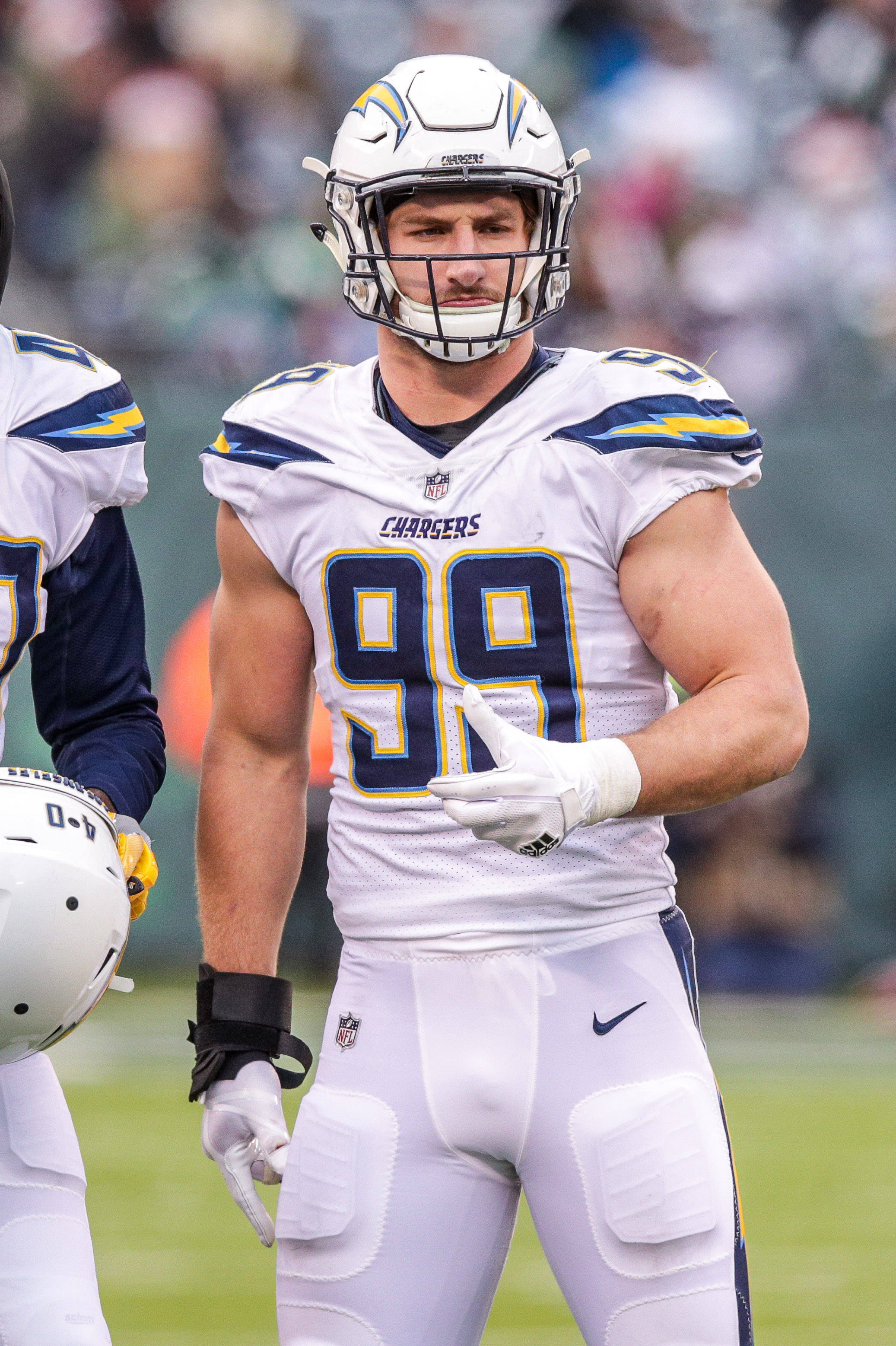足球 桌布 壁紙 — 一名專注的NFL球員身穿白色電光人球衣，號碼99，在比賽期間站在綠色球場上。