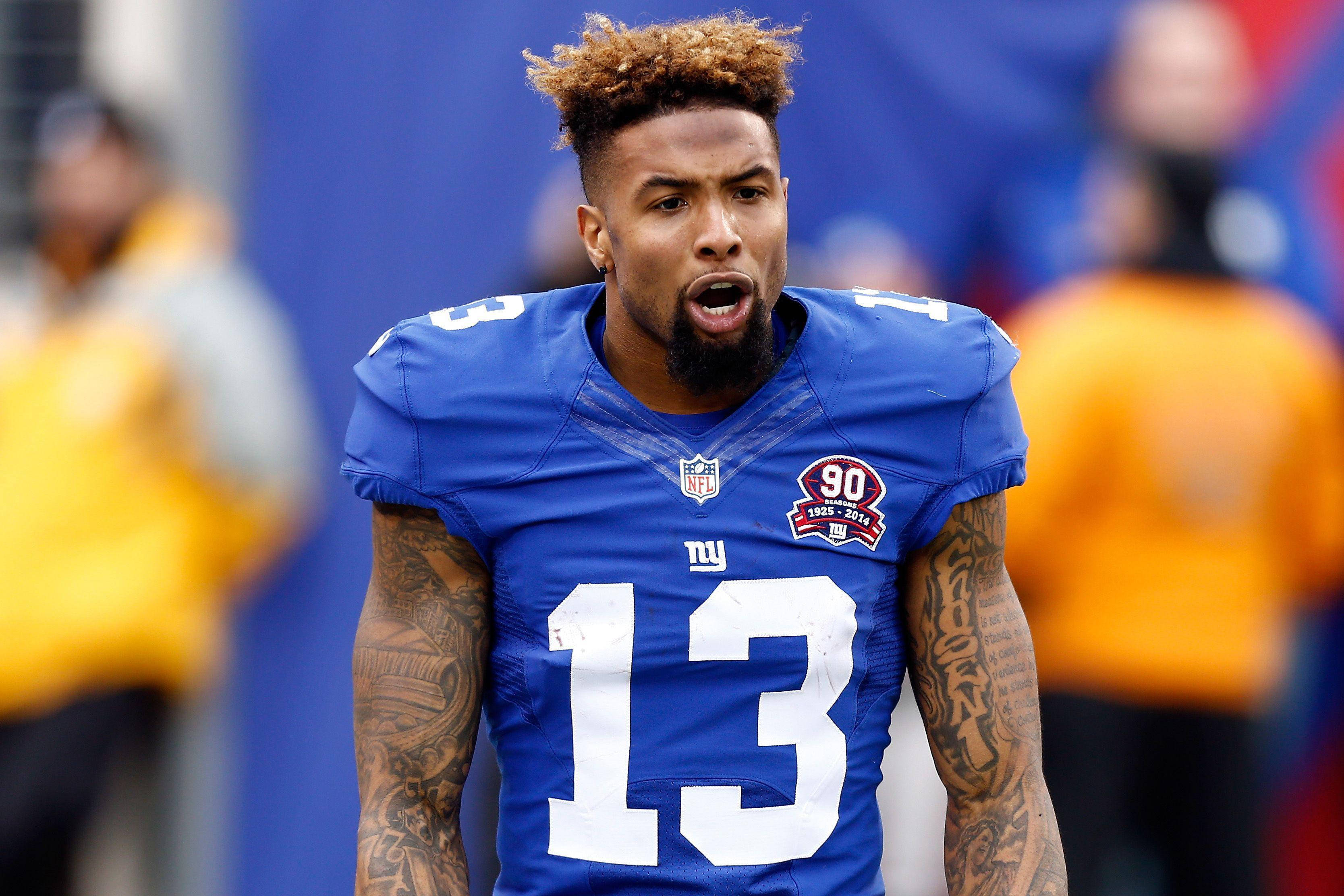 Odell 桌布 壁紙 — 一名專注的NFL球員身穿藍色13號球衣，在模糊的體育場背景下比賽中大喊。
