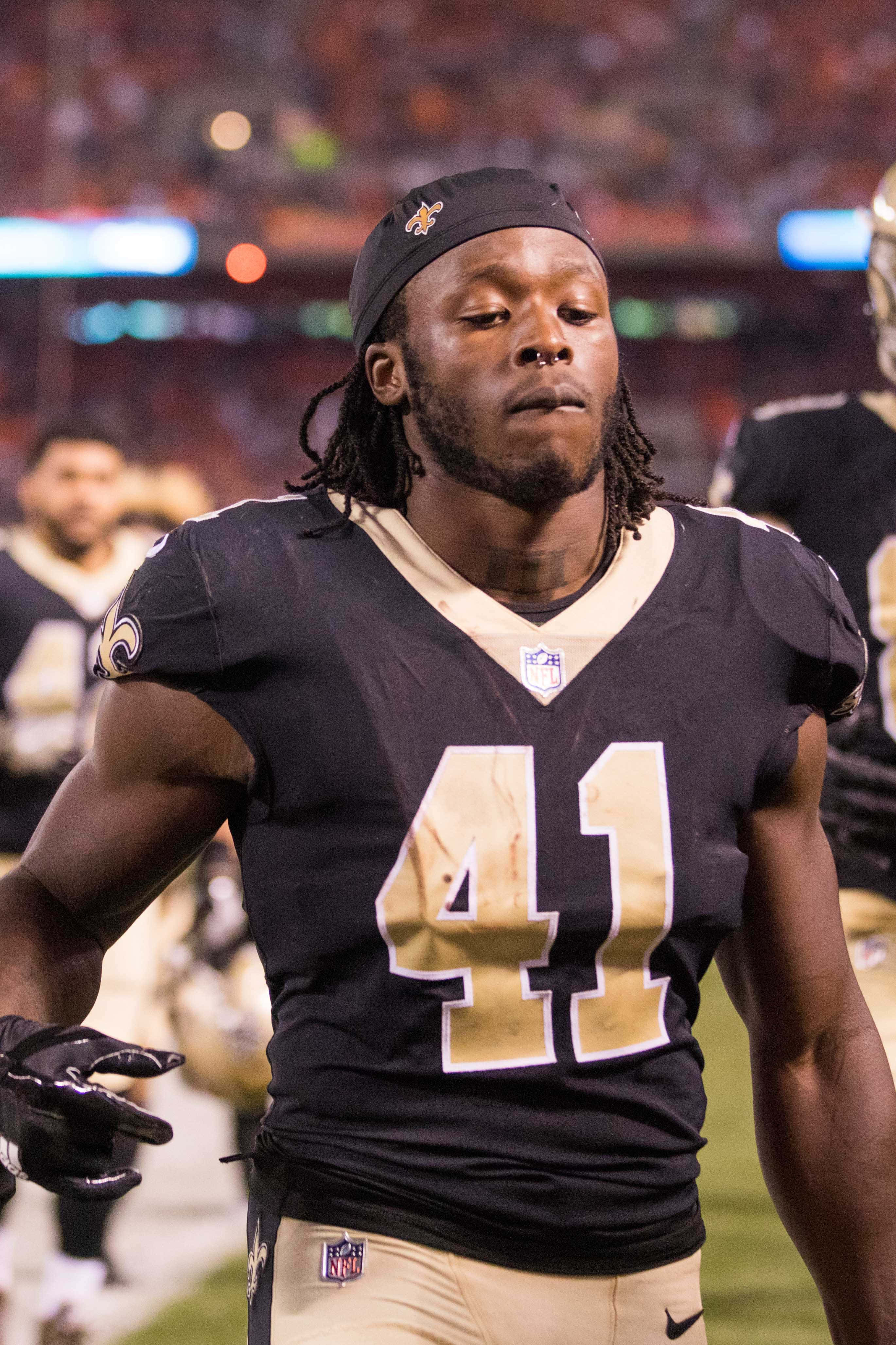 Alvin Kamara 桌布 壁紙 — 一名專注的NFL美式足球員，身穿黑色和金色球衣，號碼41，在球場燈光下走進球場。