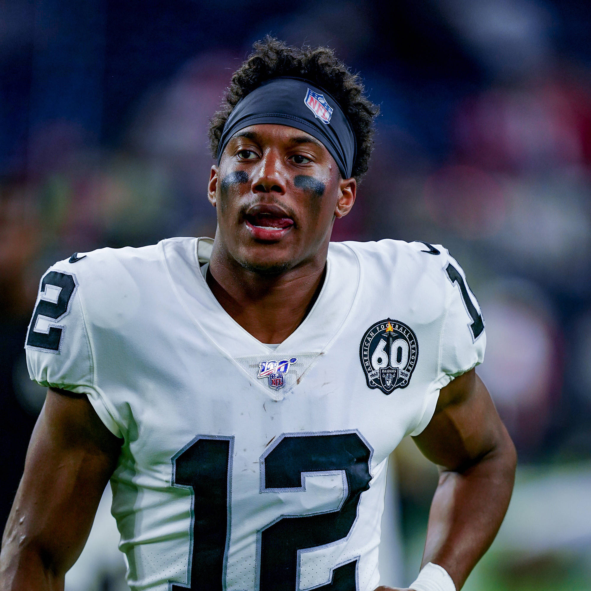 zay jones 桌布 壁紙 — 一名專注的NFL美式足球員，身穿白色12號球衣，臉上塗有黑色顏料，在球場燈光下比賽中凝視前方。