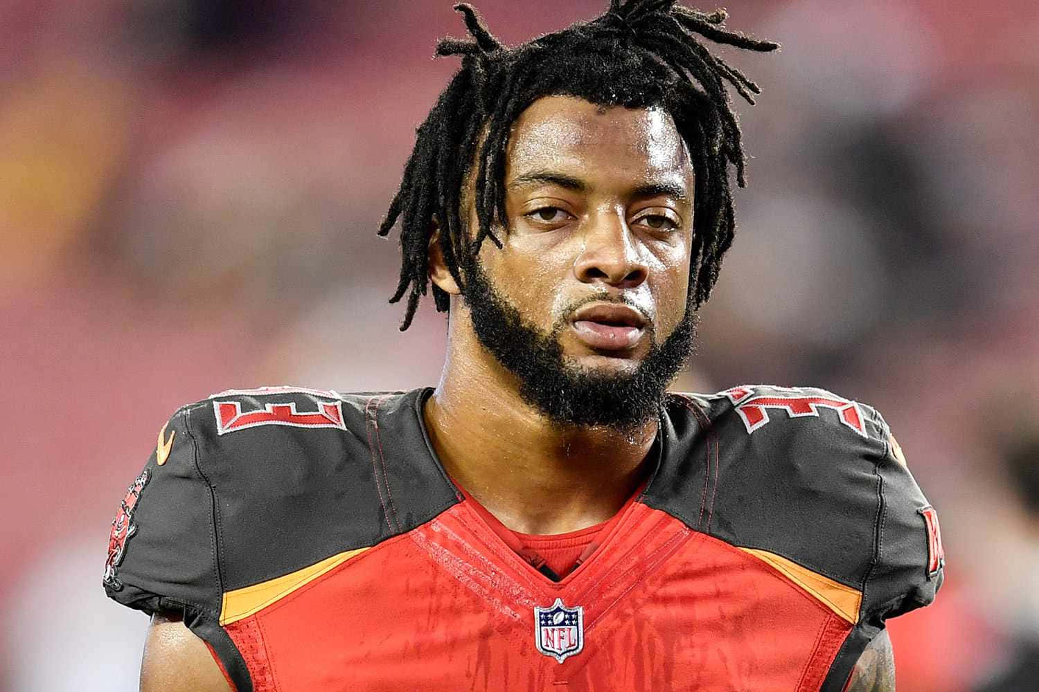 坦帕灣海盜 桌布 壁紙 — 一名專注的NFL美式足球員近照，蓄有辮子頭和鬍鬚，身穿紅黑配色的坦帕灣海盜隊球衣。