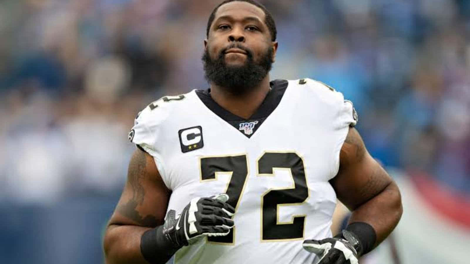 運動 桌布 壁紙 — 一名專注的NFL進攻截鋒身穿白色72號球衣，在比賽期間站在體育場上。