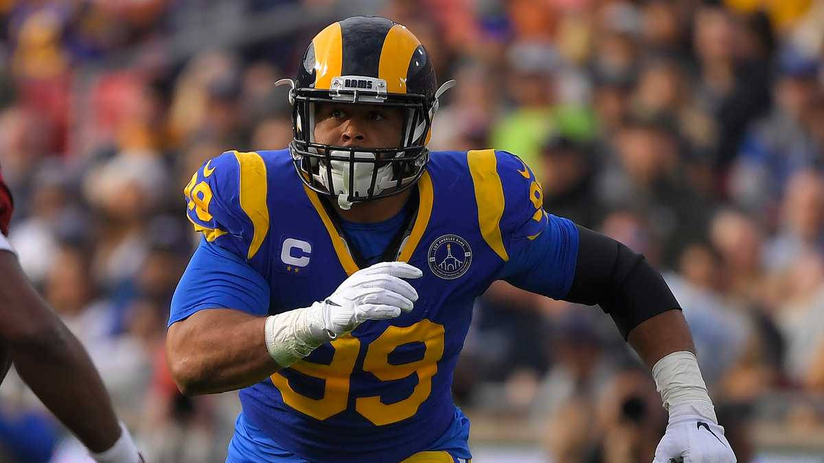 運動 桌布 壁紙 — 一名專注的NFL防守截鋒身穿藍金色公羊隊球衣，在日間比賽中衝刺，身後是模糊的體育場人群。