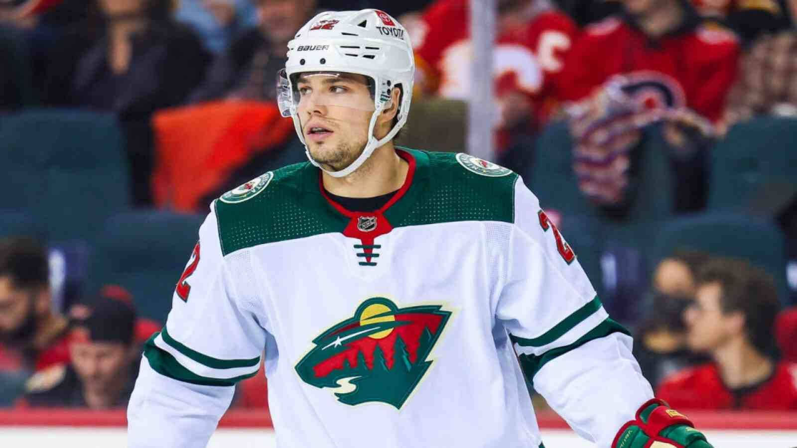 hockey 桌布 壁紙 — 一名專注的冰球運動員身穿白色、綠色和紅色的明尼蘇達野狼隊球衣，在比賽中凝視著冰面。